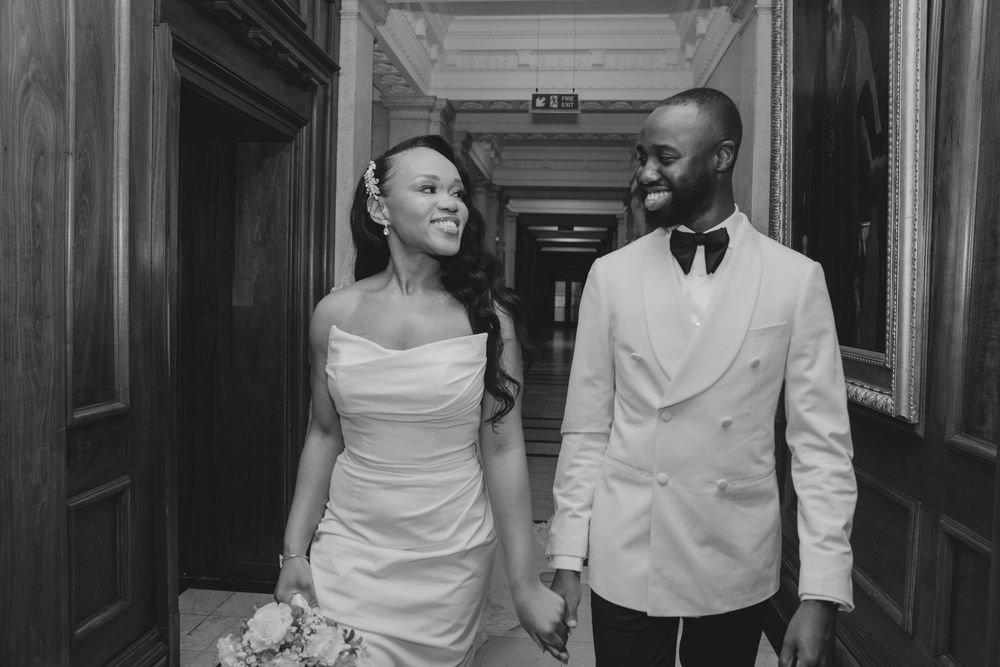 A bridesmaid and groomsman pair stand together in a hallway while taking photos at a wedding.