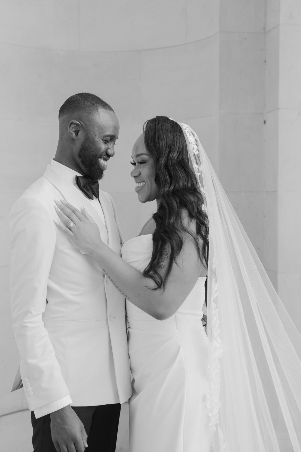 A joyful wedding couple in white attire share intimate moments in a bright minimalist setting.