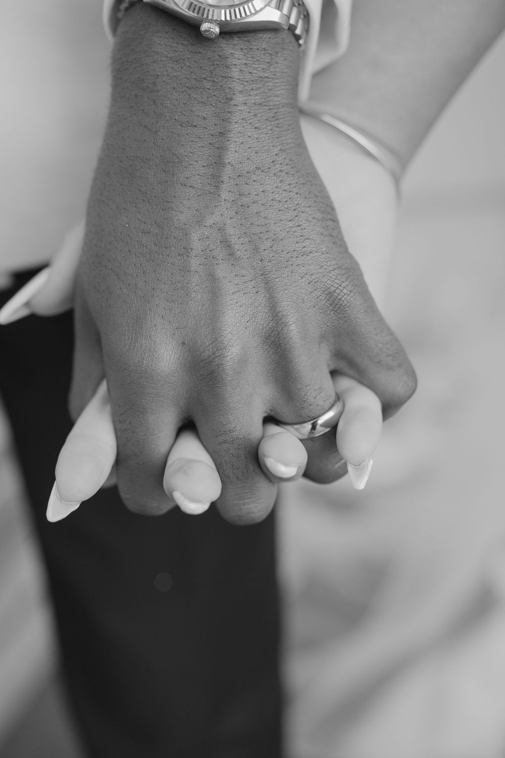 Black and white close-up image of people holding hands in a row showing wedding rings.