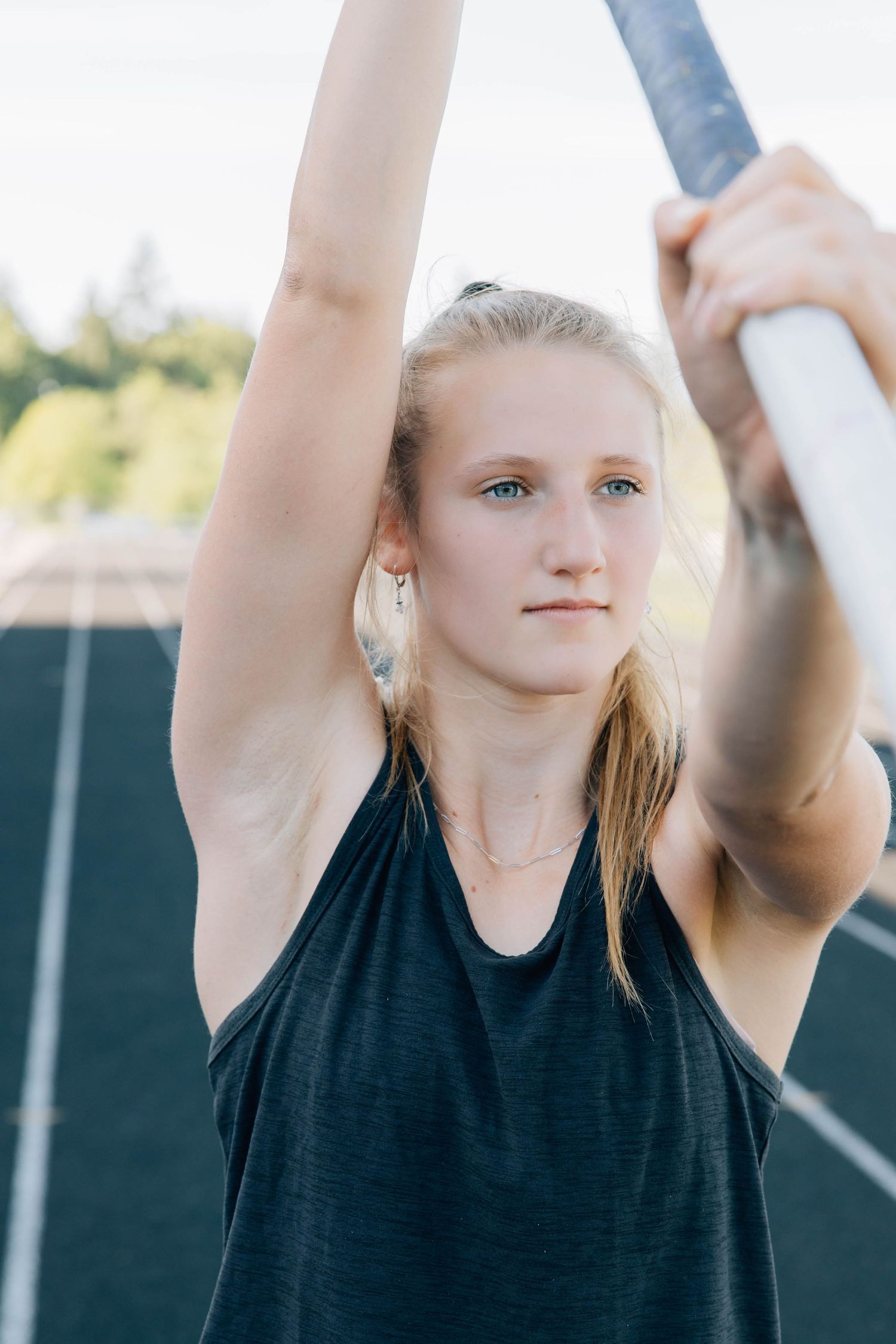 Young female athlete holding a pole vault above her head on an outdoor track.