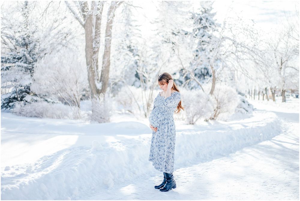 Figure in a blue floral dress stands in a serene snow-covered landscape with frost-covered trees in the background.