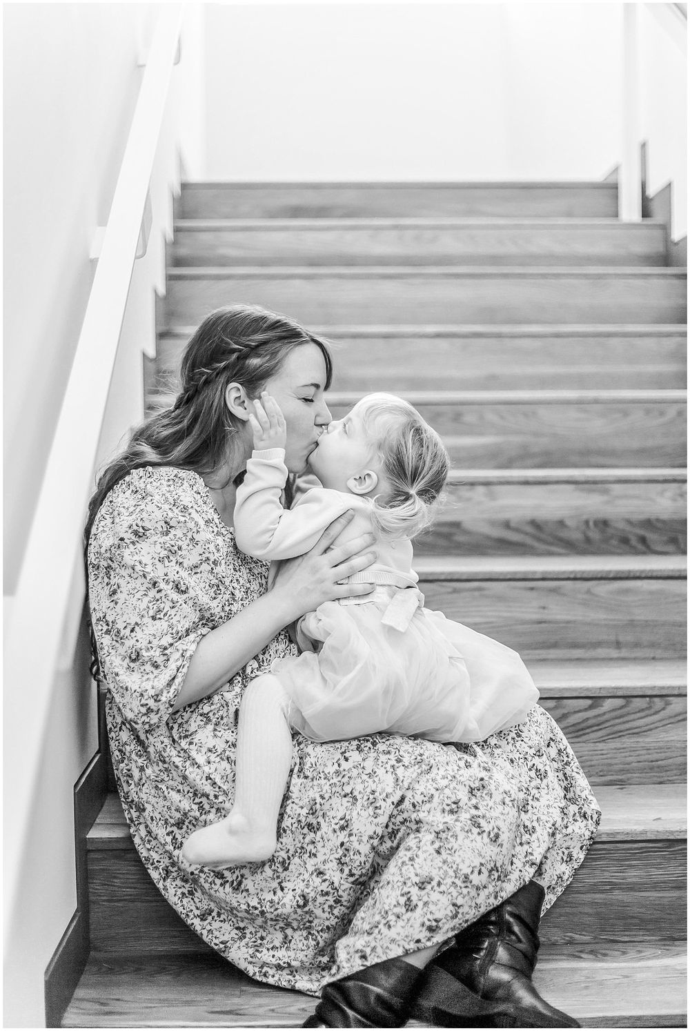 A tender black and white portrait shows a loving embrace on wooden stairs, with both figures wearing floral dresses.