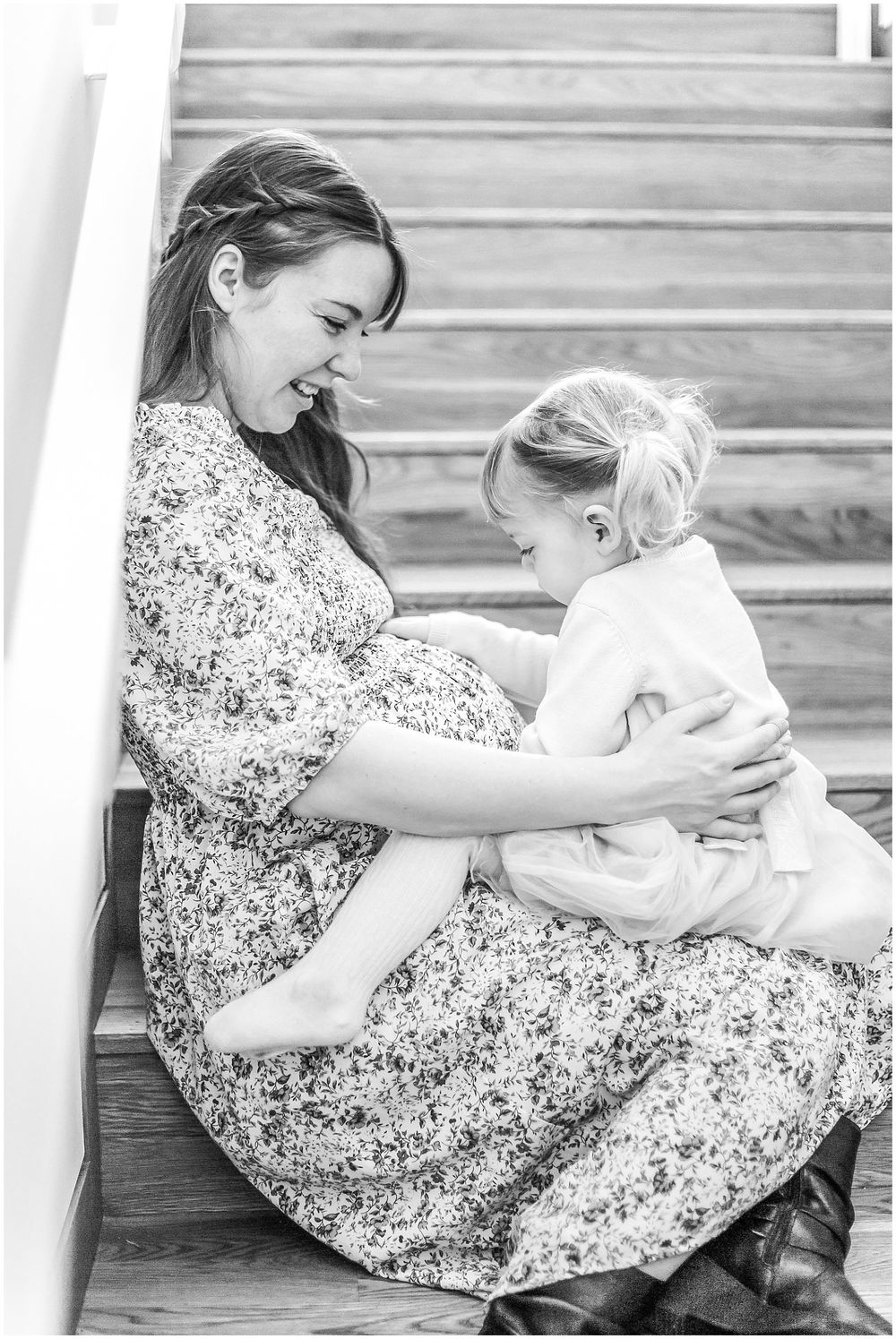 A tender black and white portrait of a mother and child sitting together on wooden stairs.