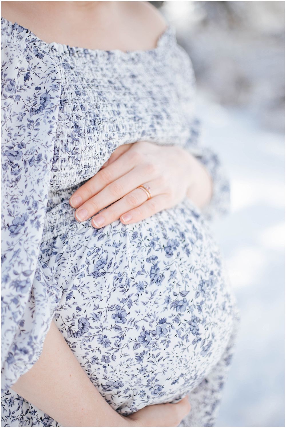 Close-up of hands resting on a baby bump covered in a blue and white floral dress.