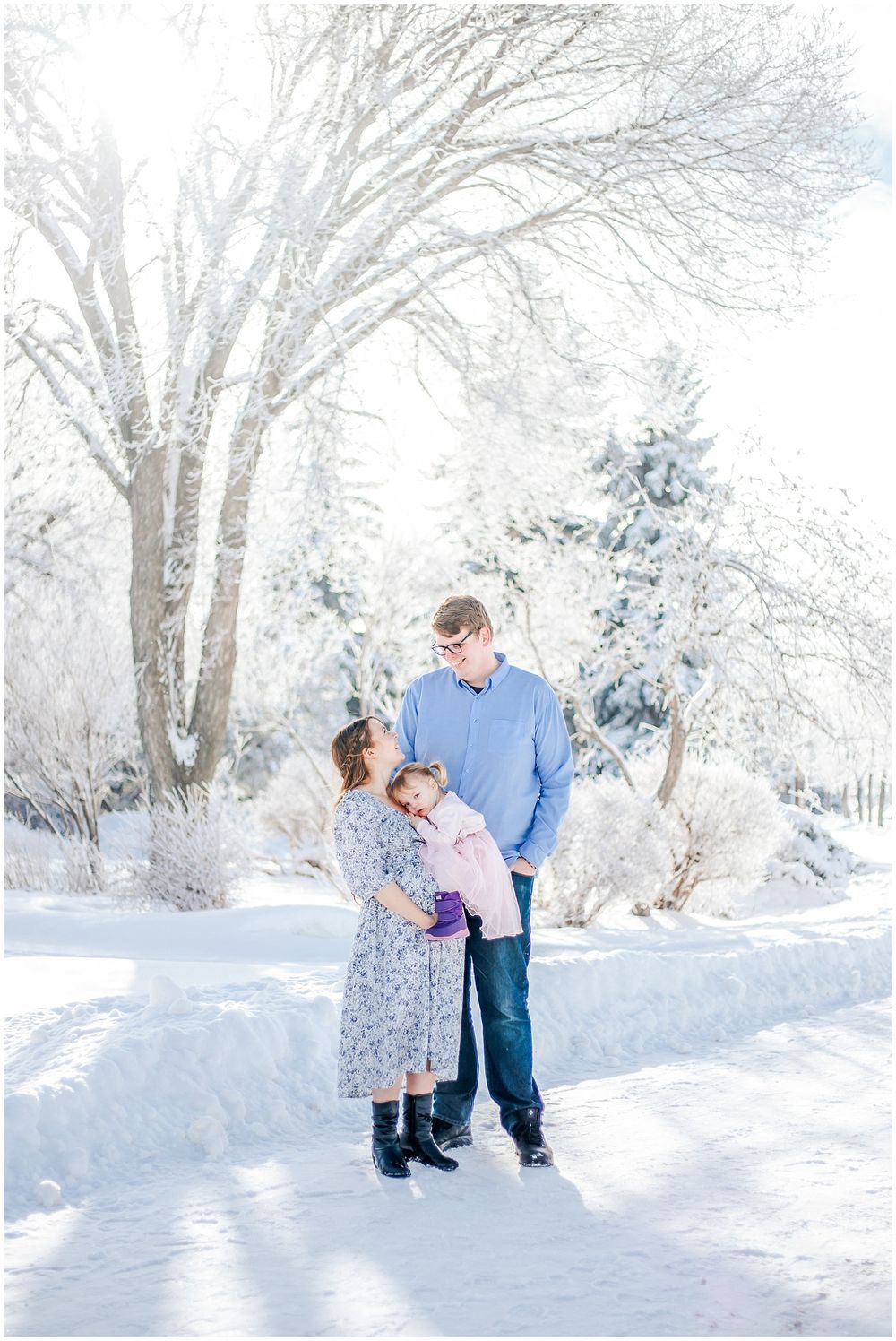 Three people sharing a tender moment together in a snowy winter wonderland setting with frost-covered trees.
