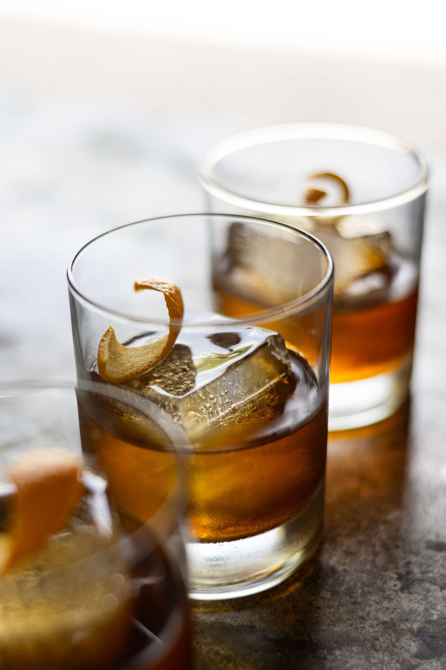 Two glasses of bourbon cocktails with ice cubes on wooden surface.