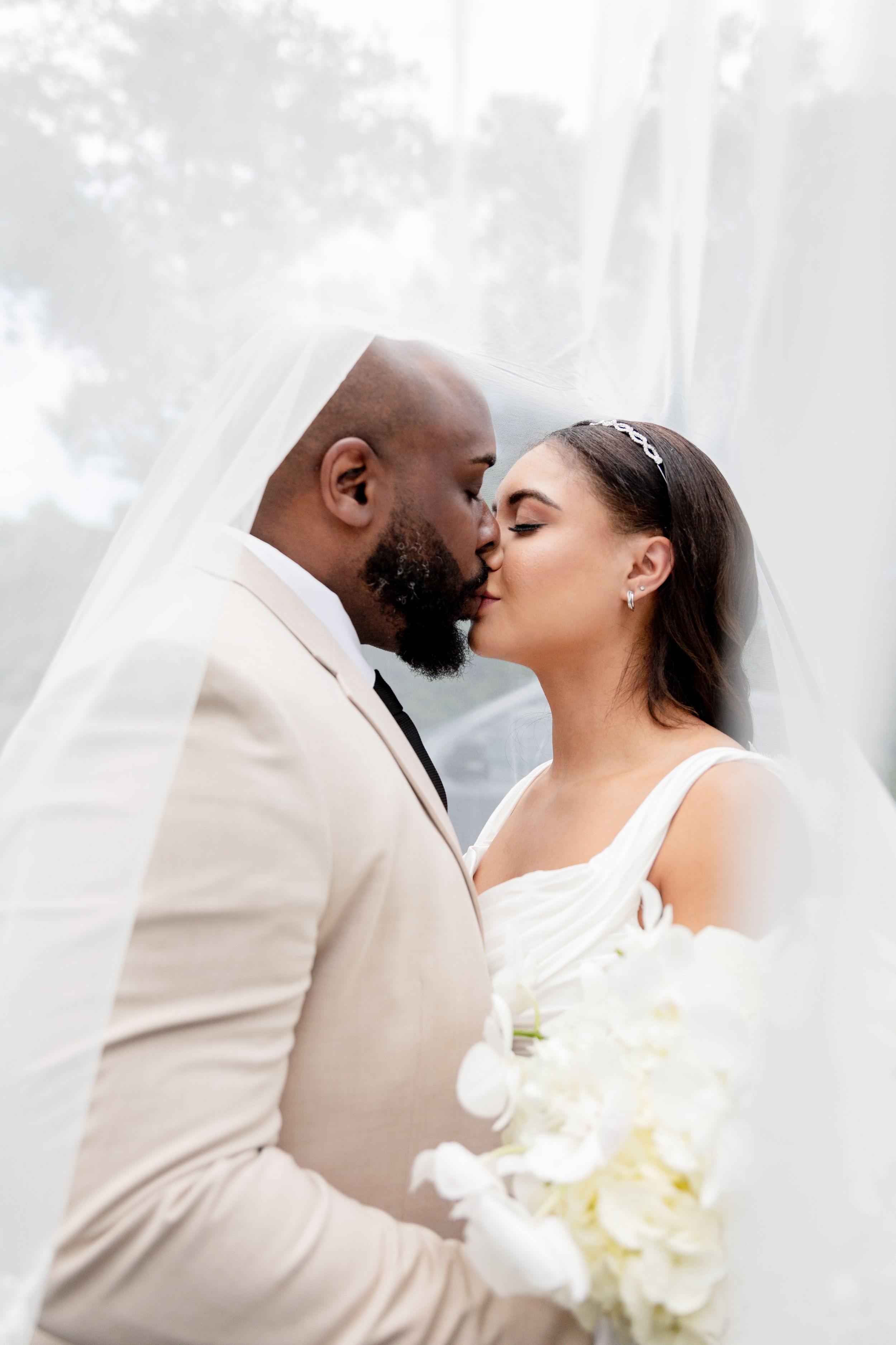 Bride and groom share an intimate moment against a bright white background with delicate veil details.