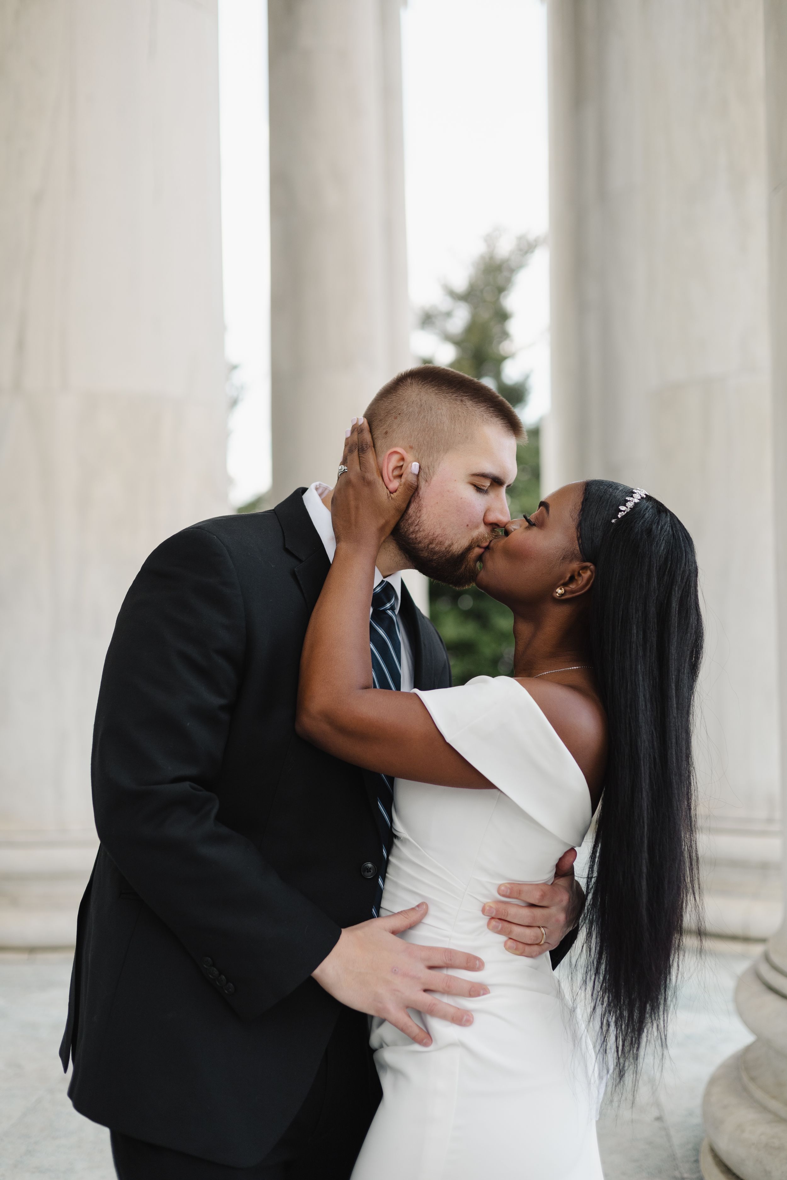 Romantic wedding couple sharing intimate kisses against white marble columns.