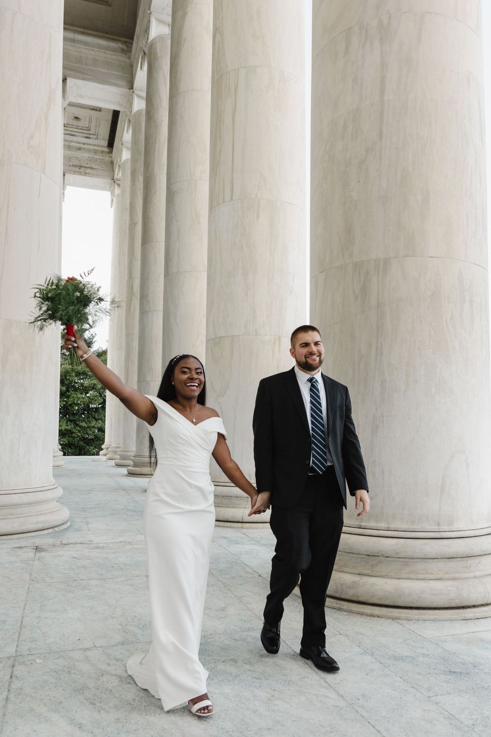 A couple poses playfully between classical white columns at a historic monument.