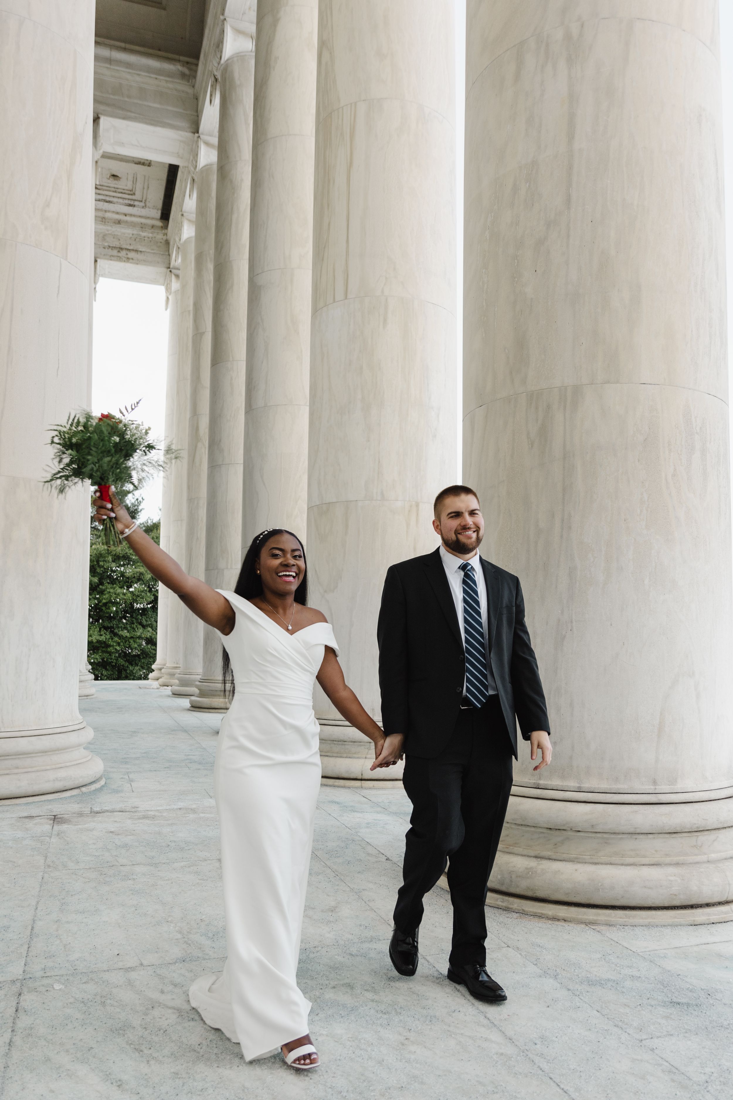 A couple poses playfully between classical white columns at a historic monument.