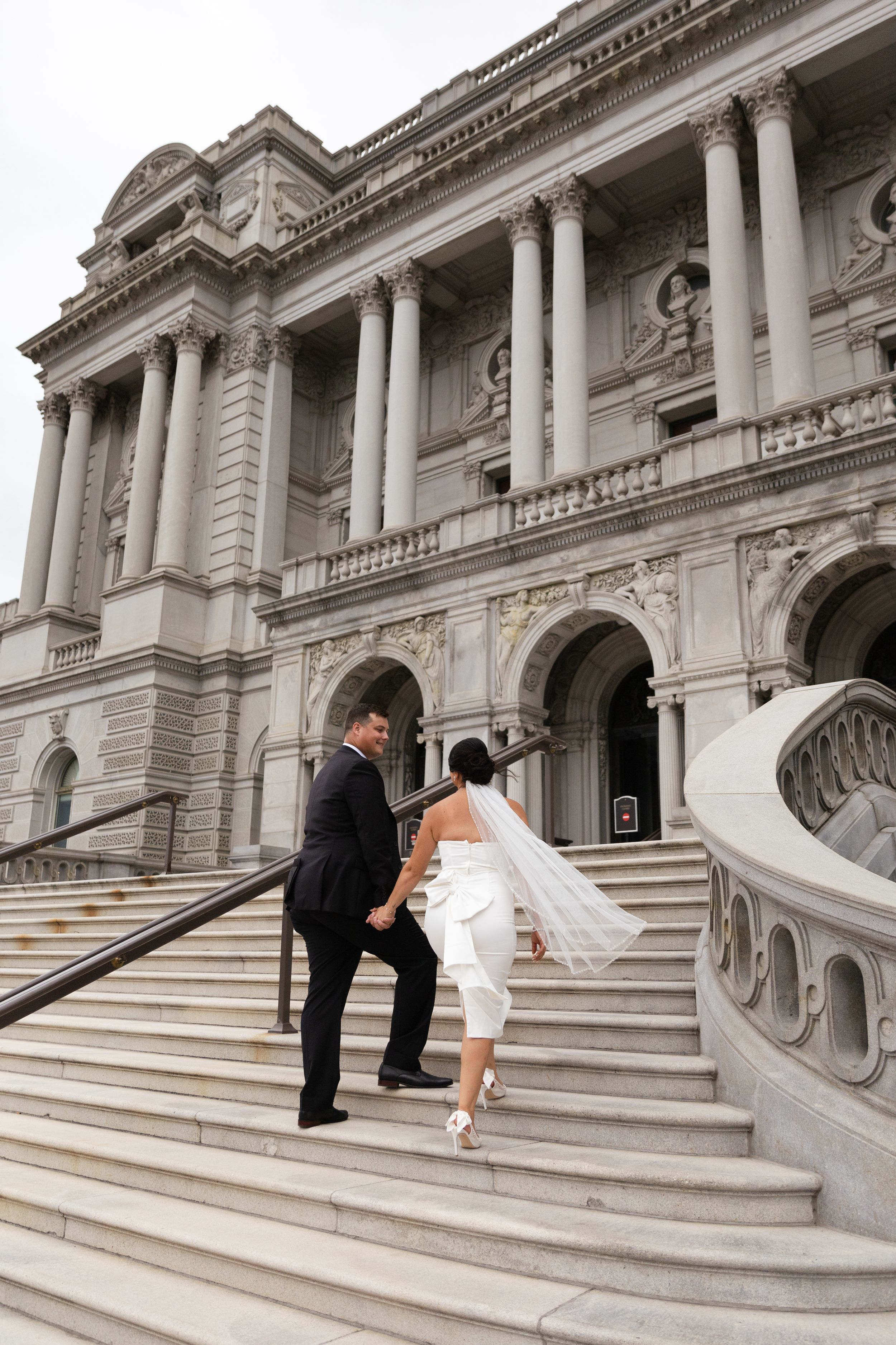 Wedding couple poses playfully on grand marble steps of historic building.