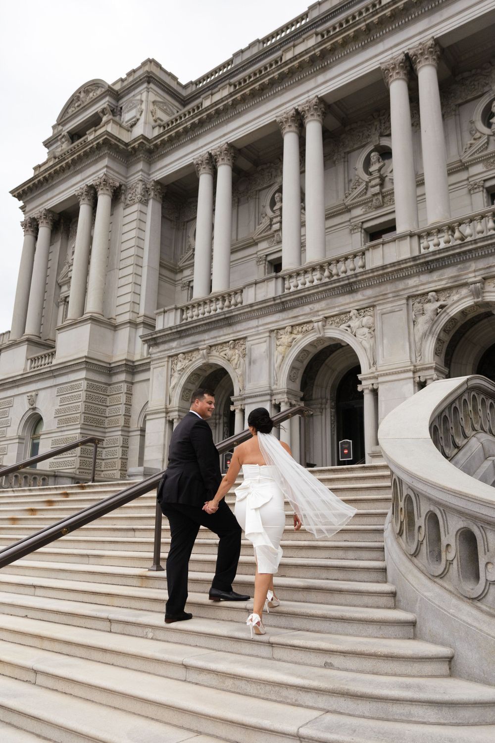 Wedding couple poses playfully on grand marble steps of historic building.