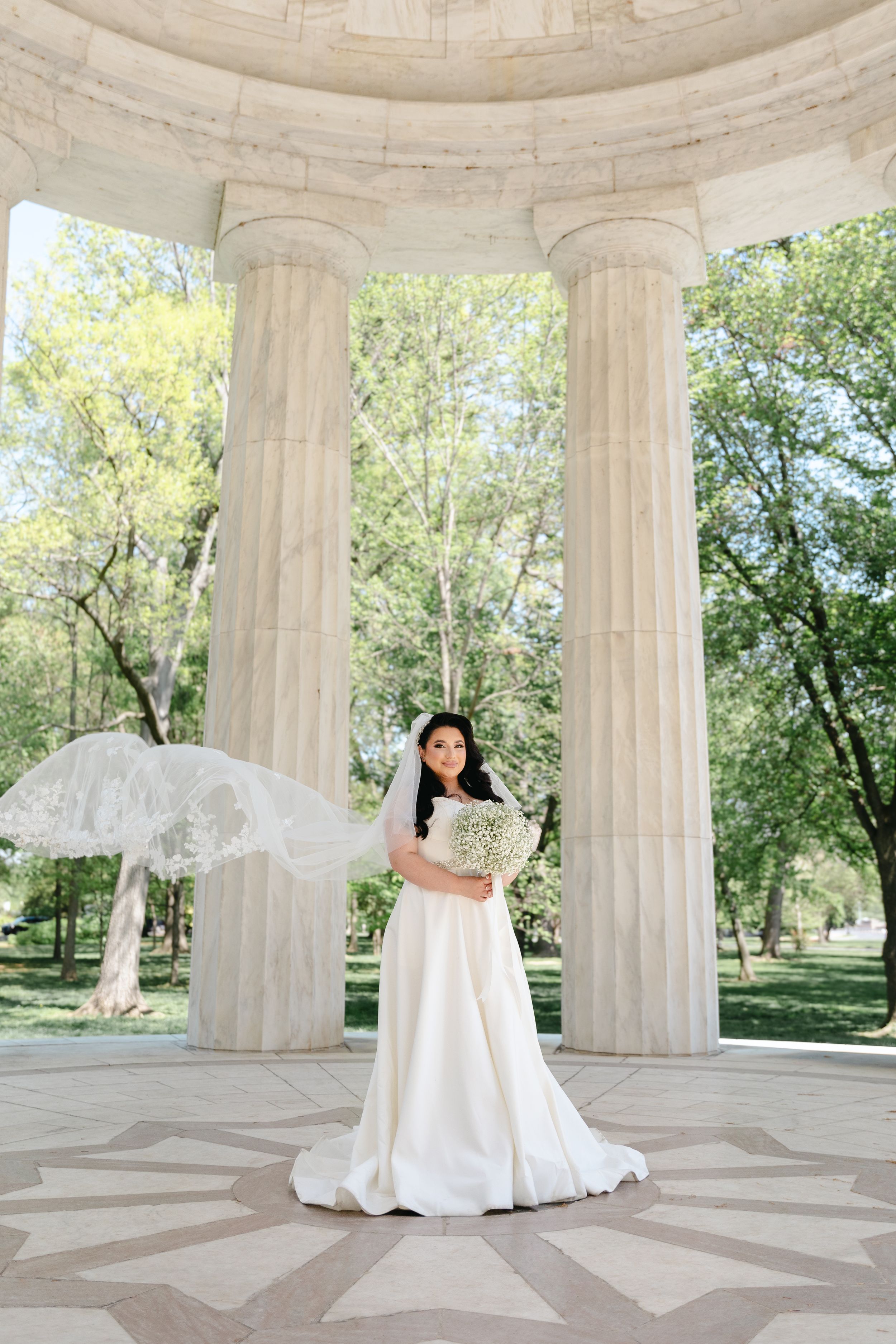 Bride spins in elegant white gown showing off dress movement in marble pavilion.