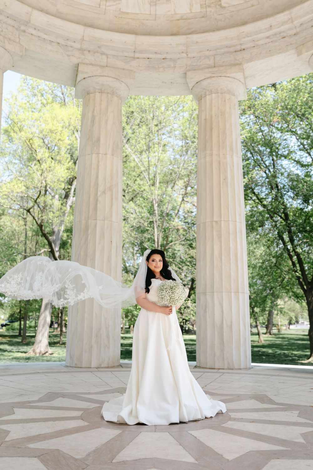Bride spins in elegant white gown showing off dress movement in marble pavilion.