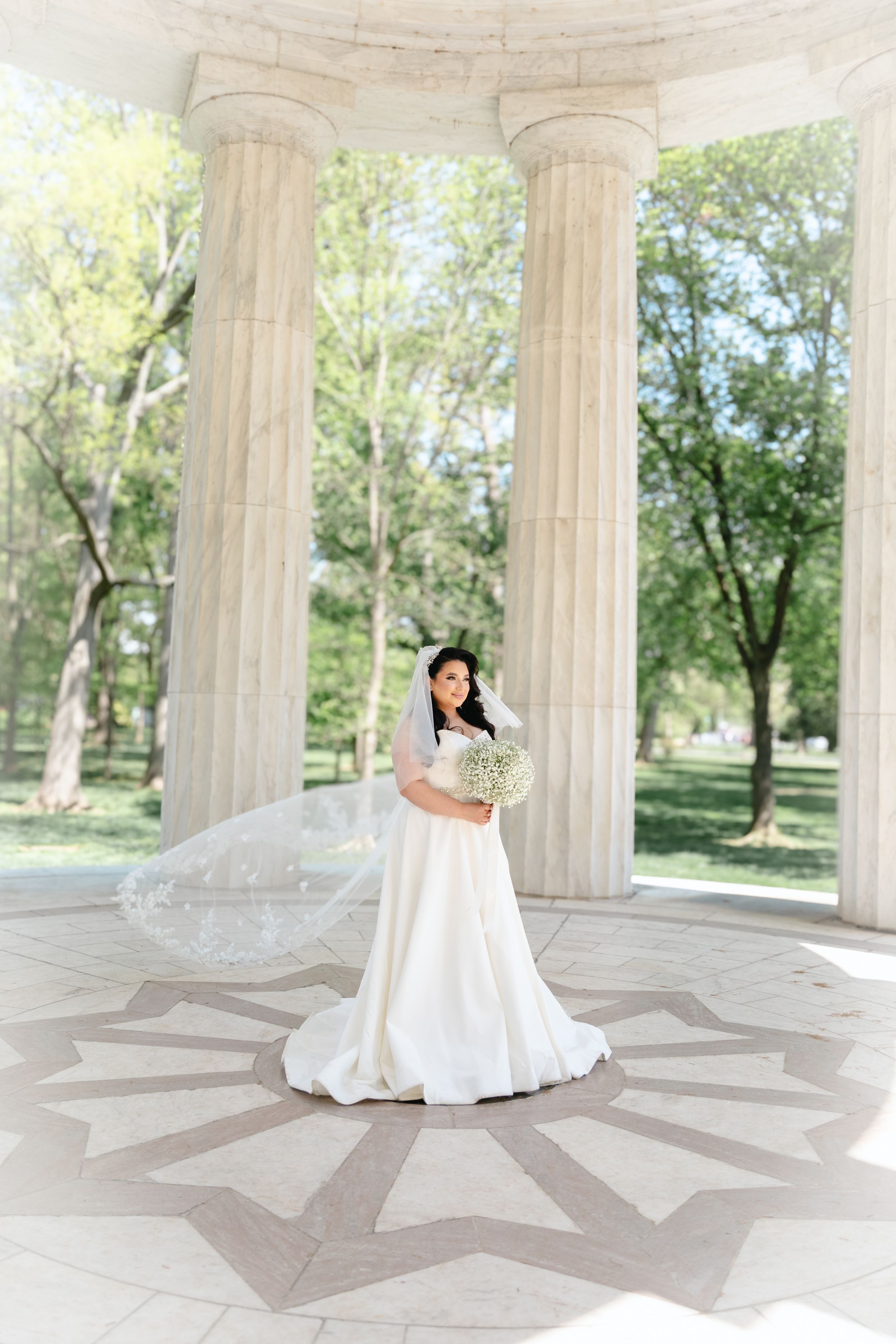Bride in flowing white dress twirls in classical columned pavilion.
