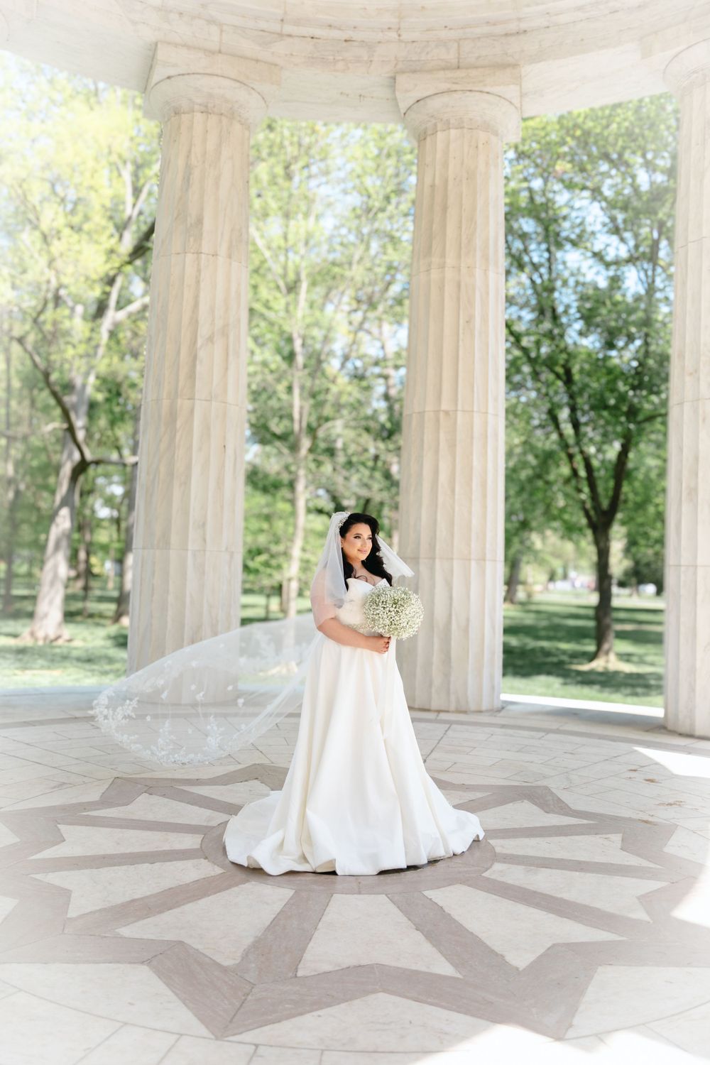 Bride in flowing white dress twirls in classical columned pavilion.
