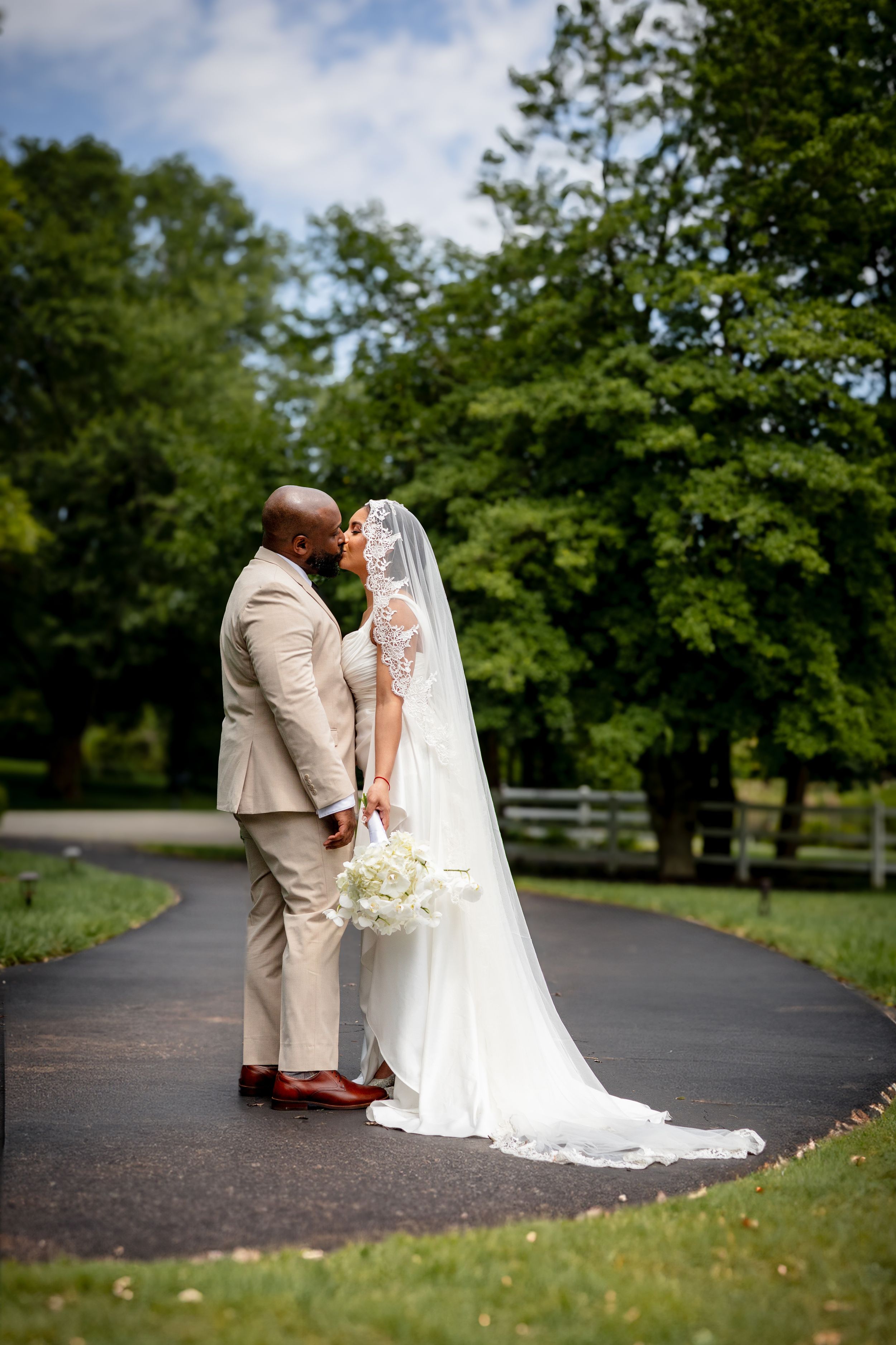 Romantic wedding couple sharing a tender moment on a tree-lined path in their formal attire.