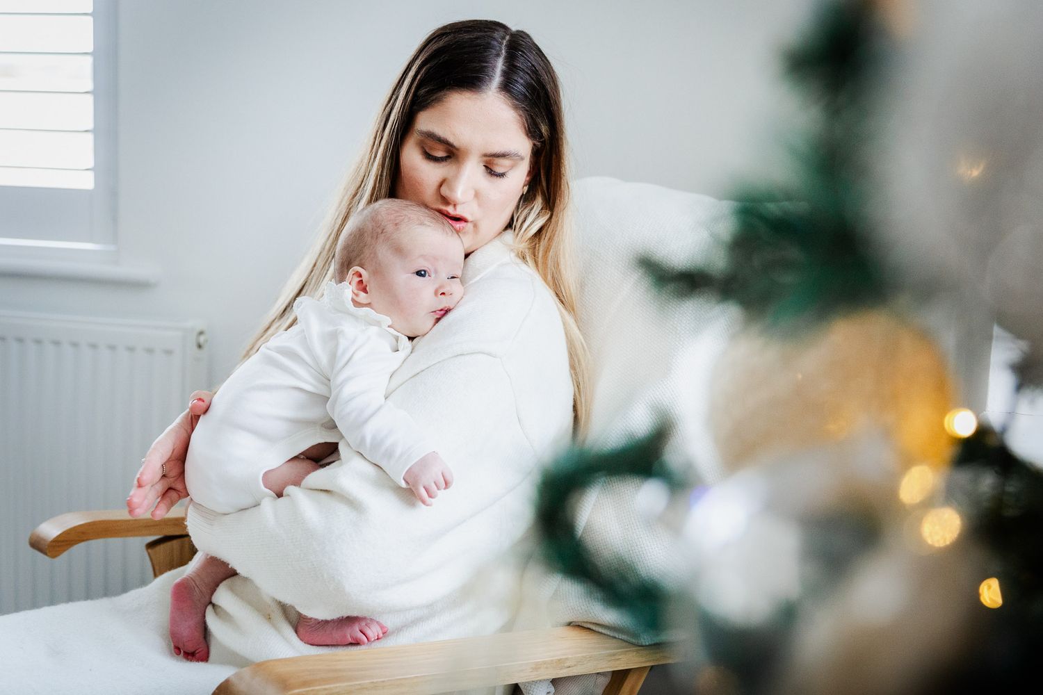 A mother soothes her baby as they sit next to the Christmas tree at home. Bristol newborn photographer