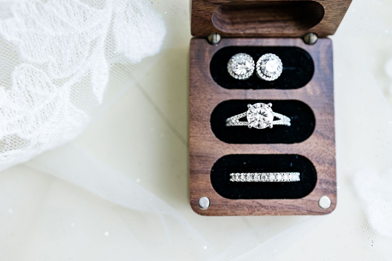 Wedding rings and engagement ring displayed in a wooden box with velvet lining.