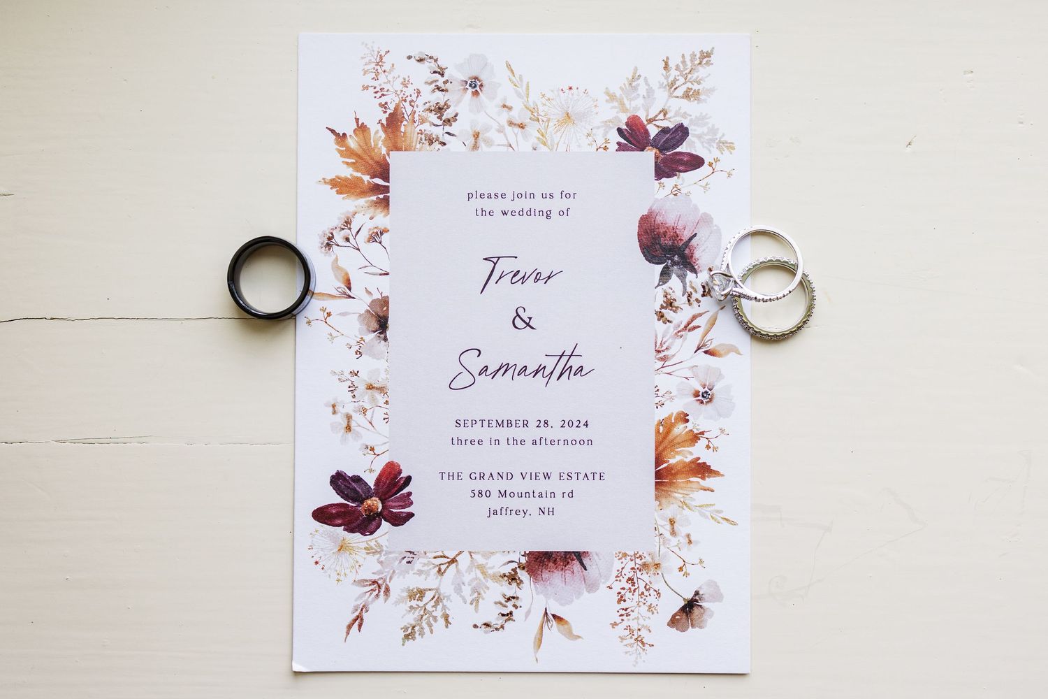 Wedding invitation with floral design and two rings on a white surface.