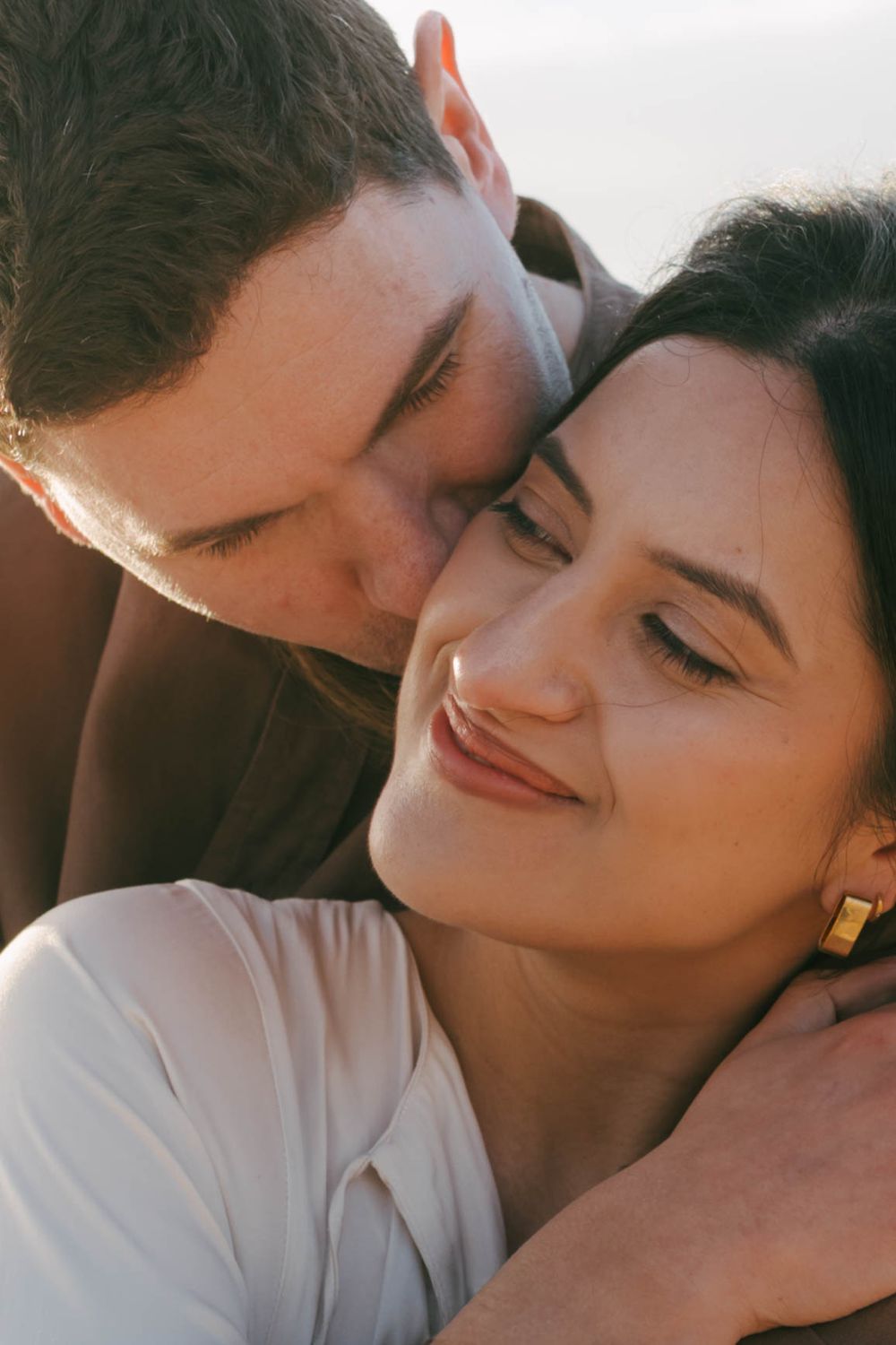 A romantic couple shares an intimate moment in warm sunlight with soft focus and natural lighting.