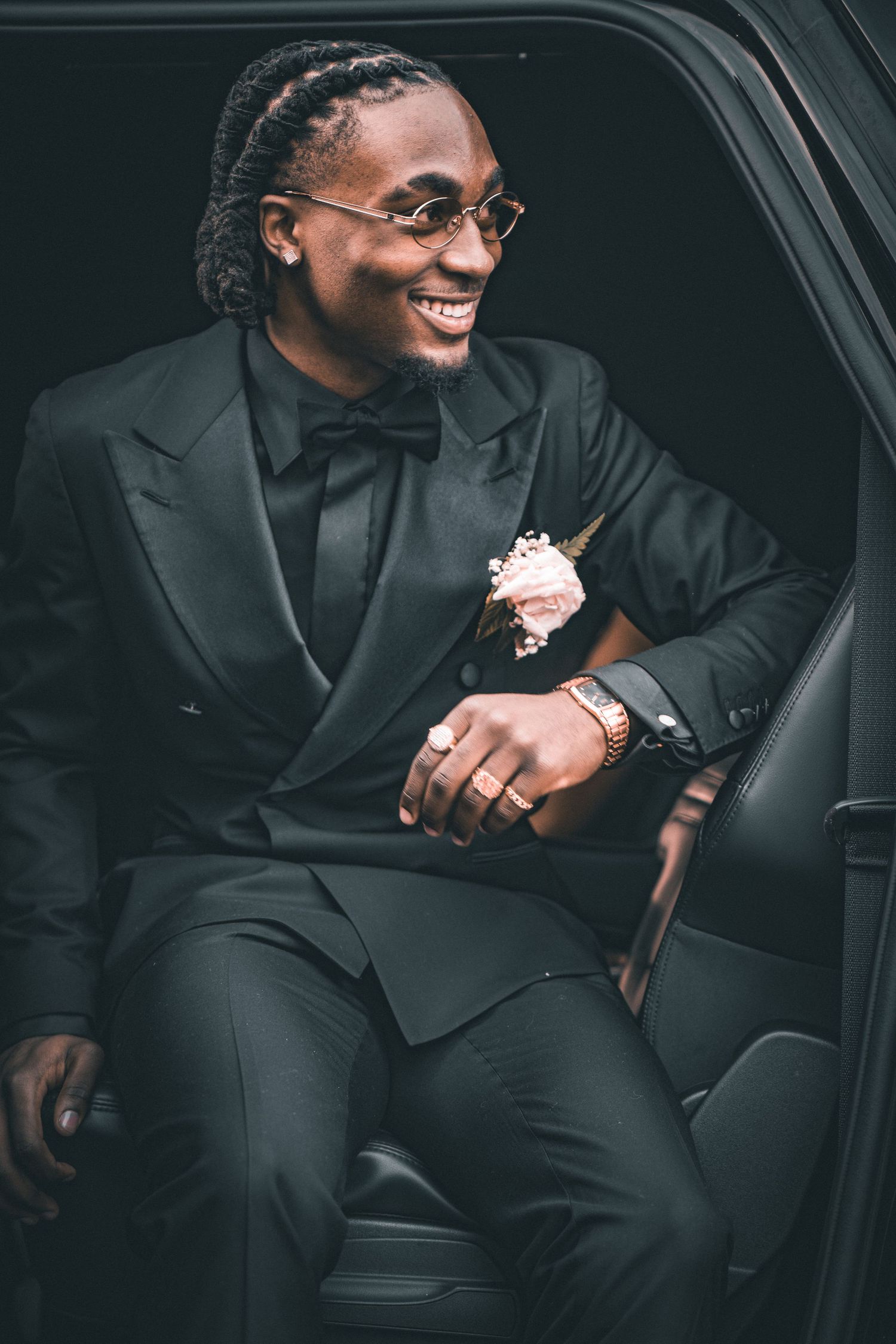 Formal portrait in black tuxedo with bow tie seated in luxury car.