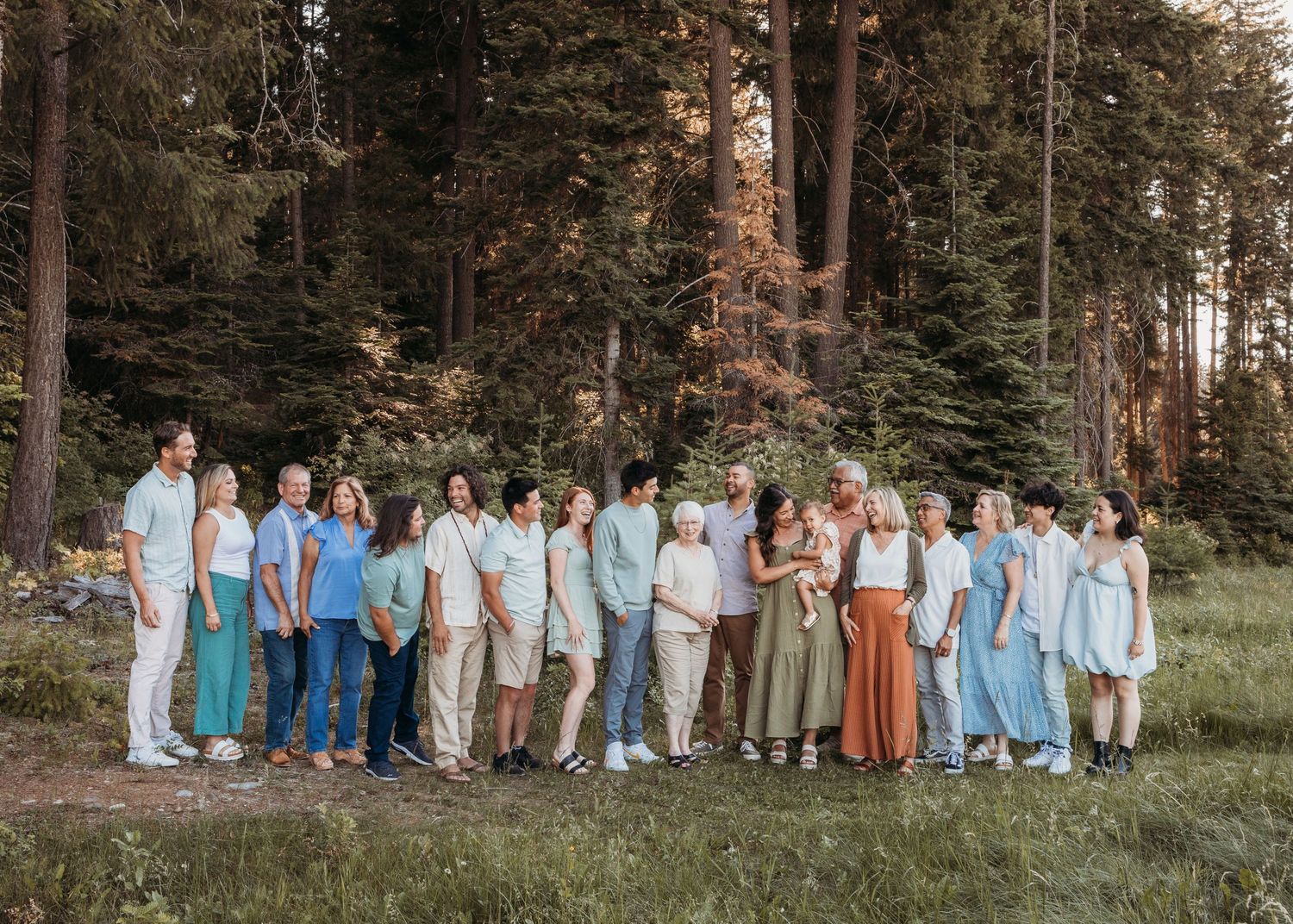 Large group posed in coordinated blue and neutral outfits against forest backdrop.