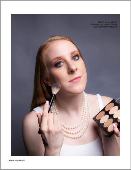 Portrait of model applying makeup with brushes while wearing pearl necklaces.