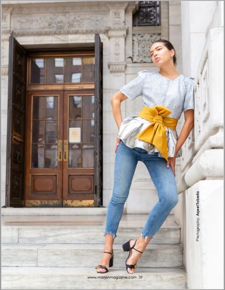 Stylish outfit featuring blue jeans and ruffled top with yellow bow detail against classic architecture.