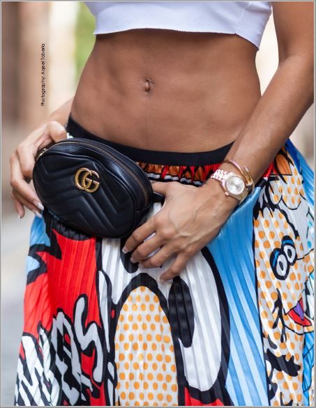 Close-up of toned midsection with Gucci belt bag and colorful print skirt.
