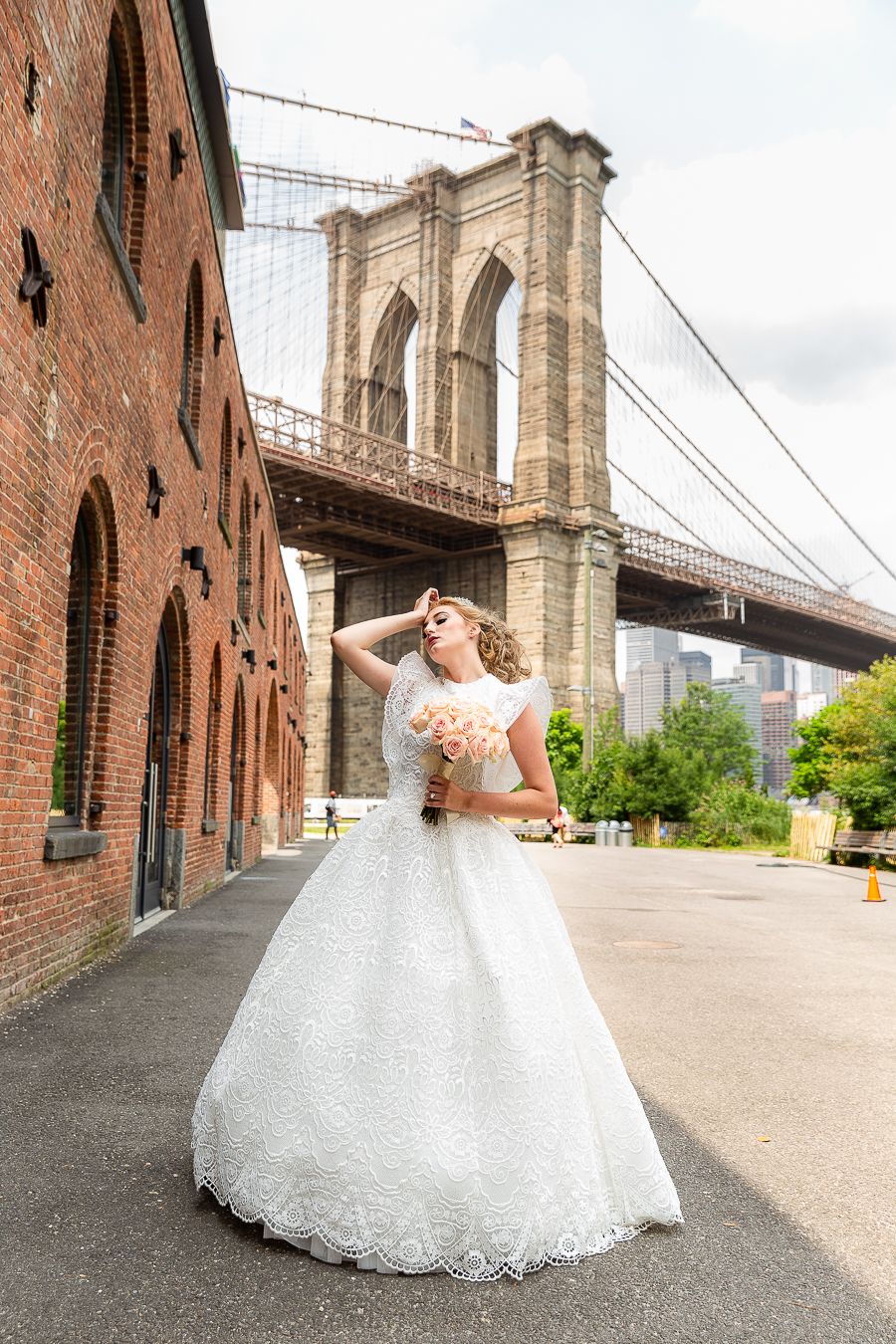 A joyful wedding photo with a flowing white dress set against historic brick architecture and the Brooklyn Bridge.