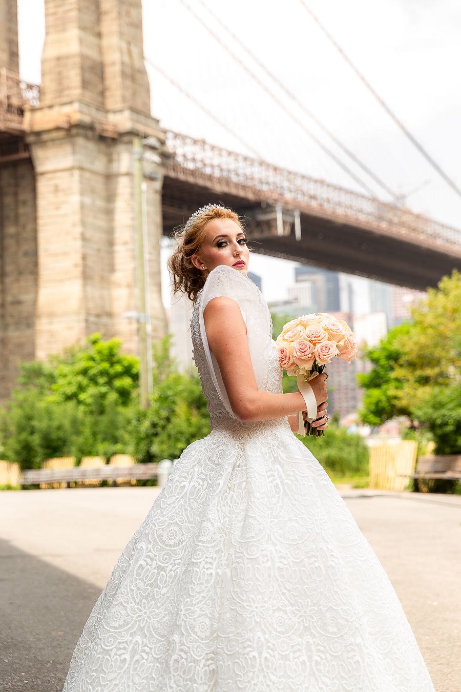 A romantic bridal portrait with peach roses near the Brooklyn Bridge featuring a detailed lace wedding gown.