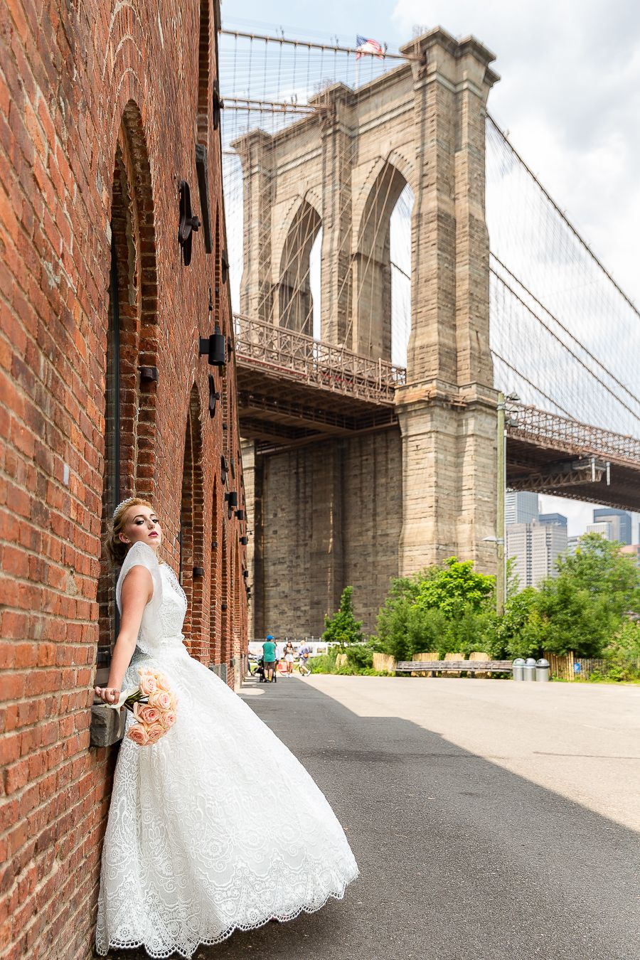 A dramatic wedding photo against red brick walls with the Brooklyn Bridge towering in the background.