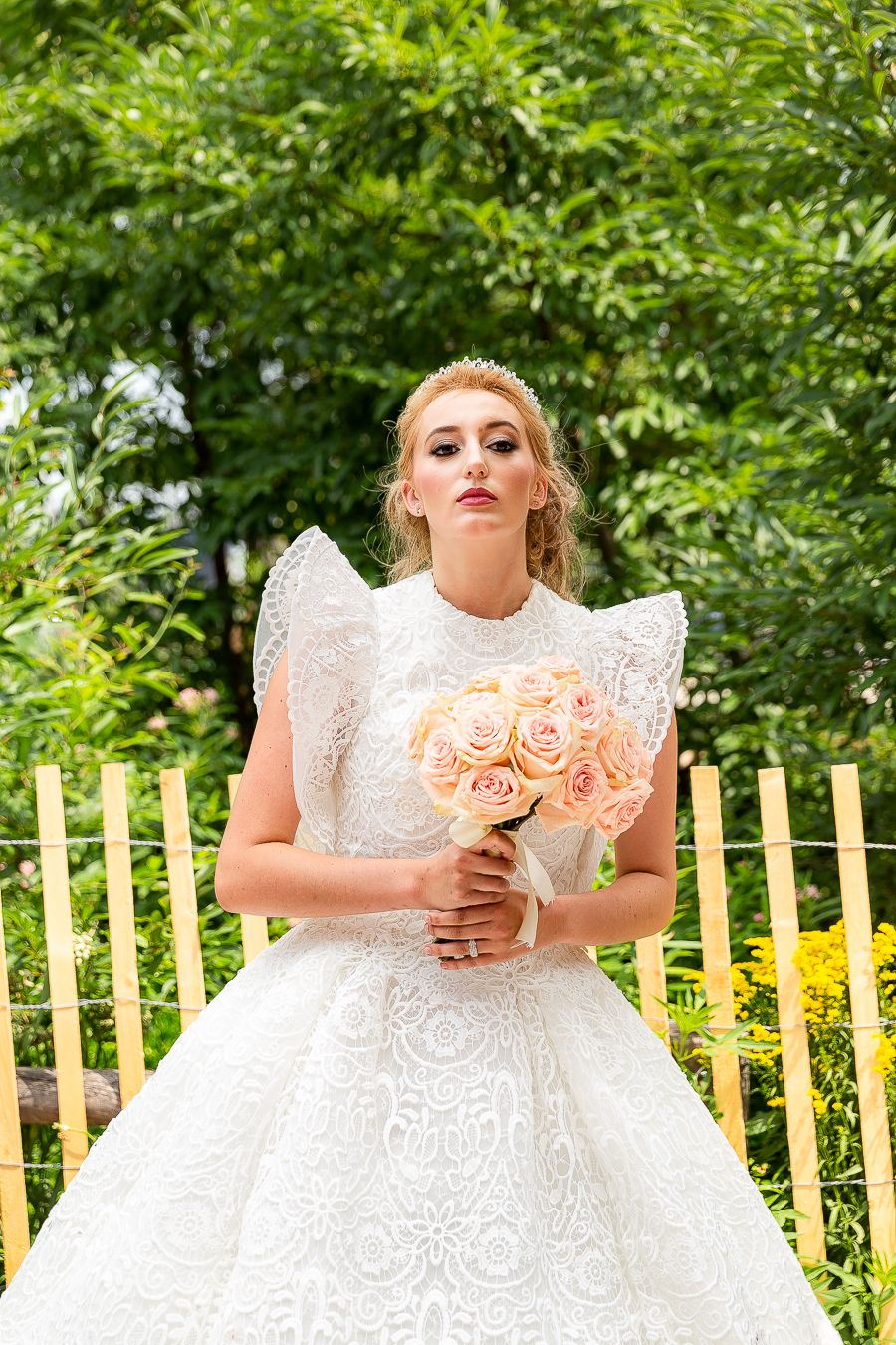 Wedding dress with dramatic flutter sleeves and peach rose bouquet in garden setting.
