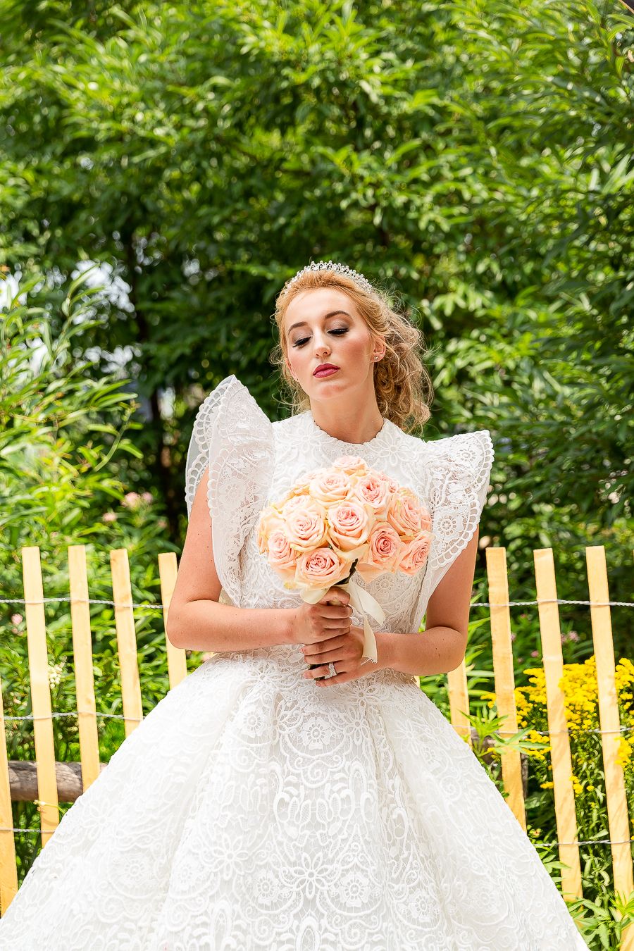 Bridal portrait with peach roses against wooden fence and lush greenery.