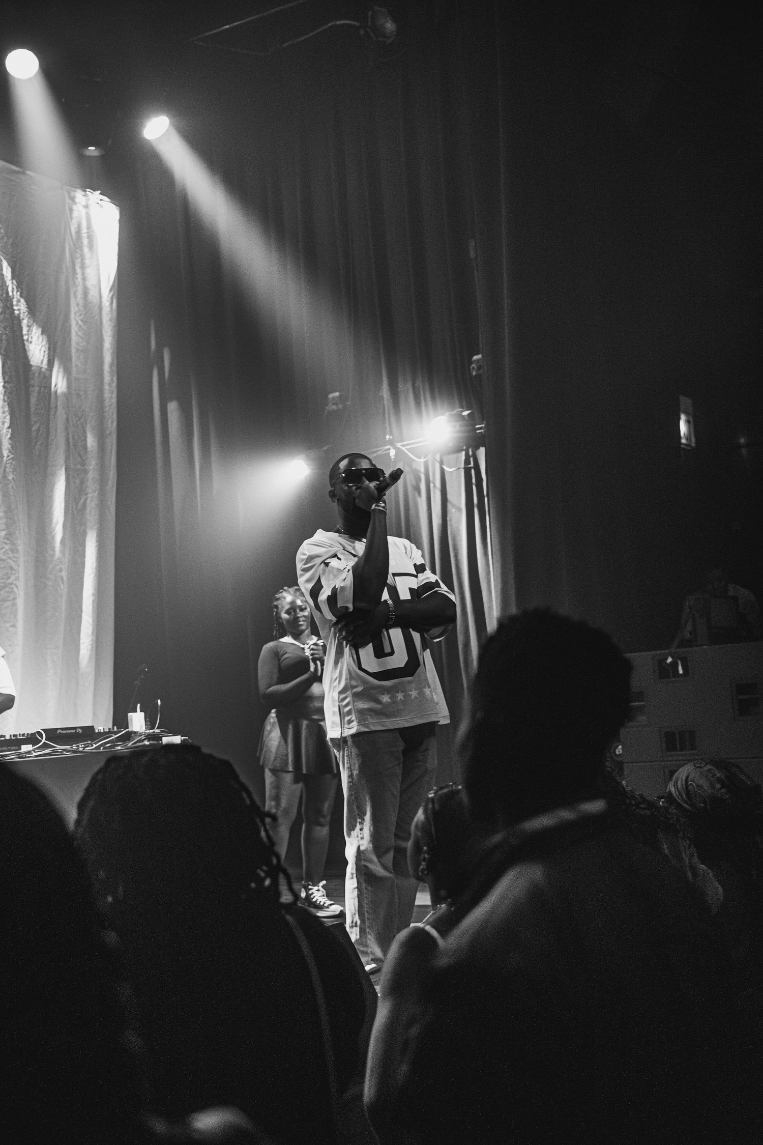 Hip hop performers on stage illuminated by dramatic spotlights during a live concert performance.