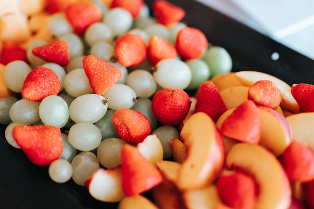 Fresh fruit platter with strawberries, green grapes, and peach slices on a dark tray.