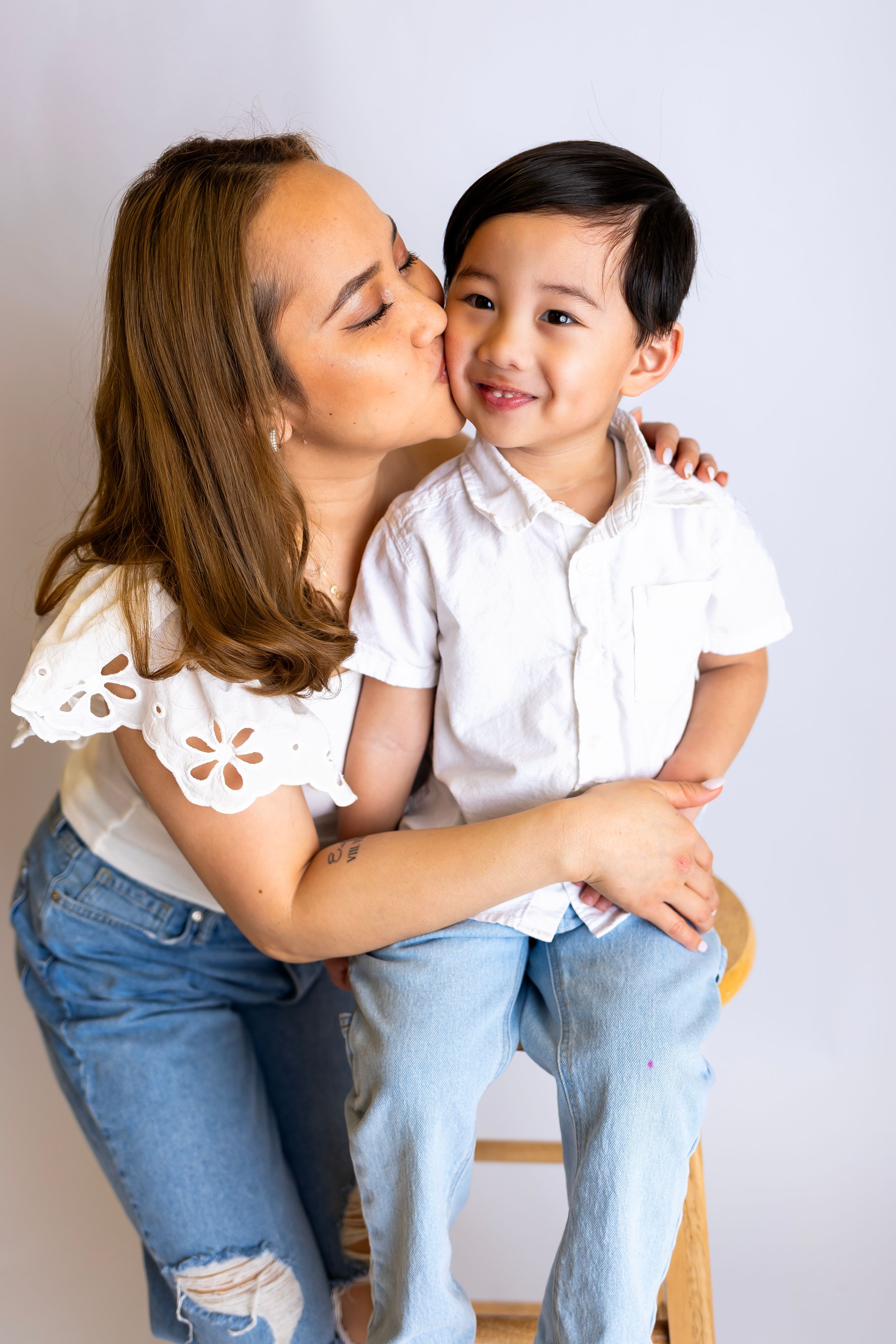 A sweet moment shows affection between a woman in a white top and jeans and a young child in casual attire.
