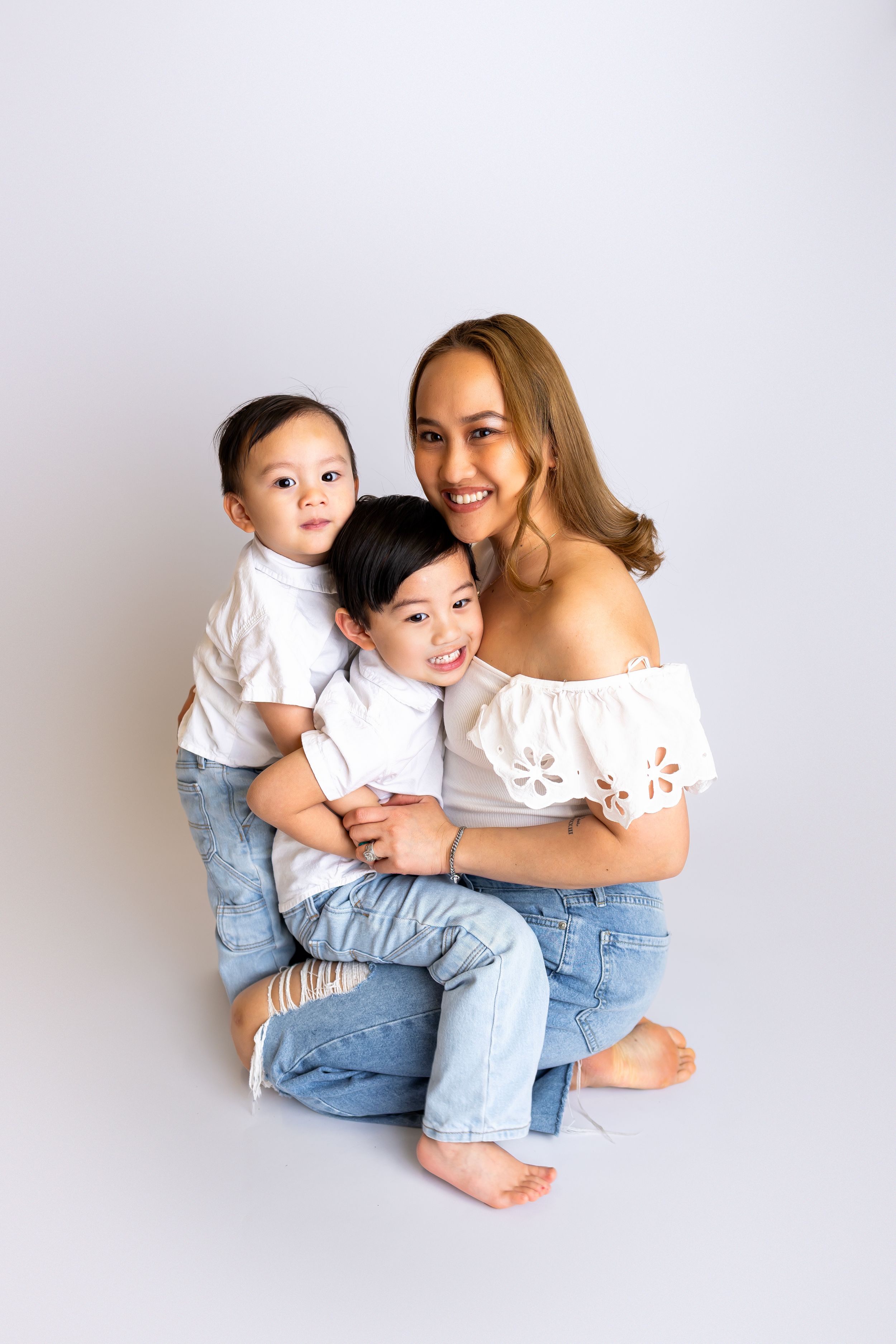 A family wearing white and blue outfits sits together on a light colored backdrop for a casual portrait session.