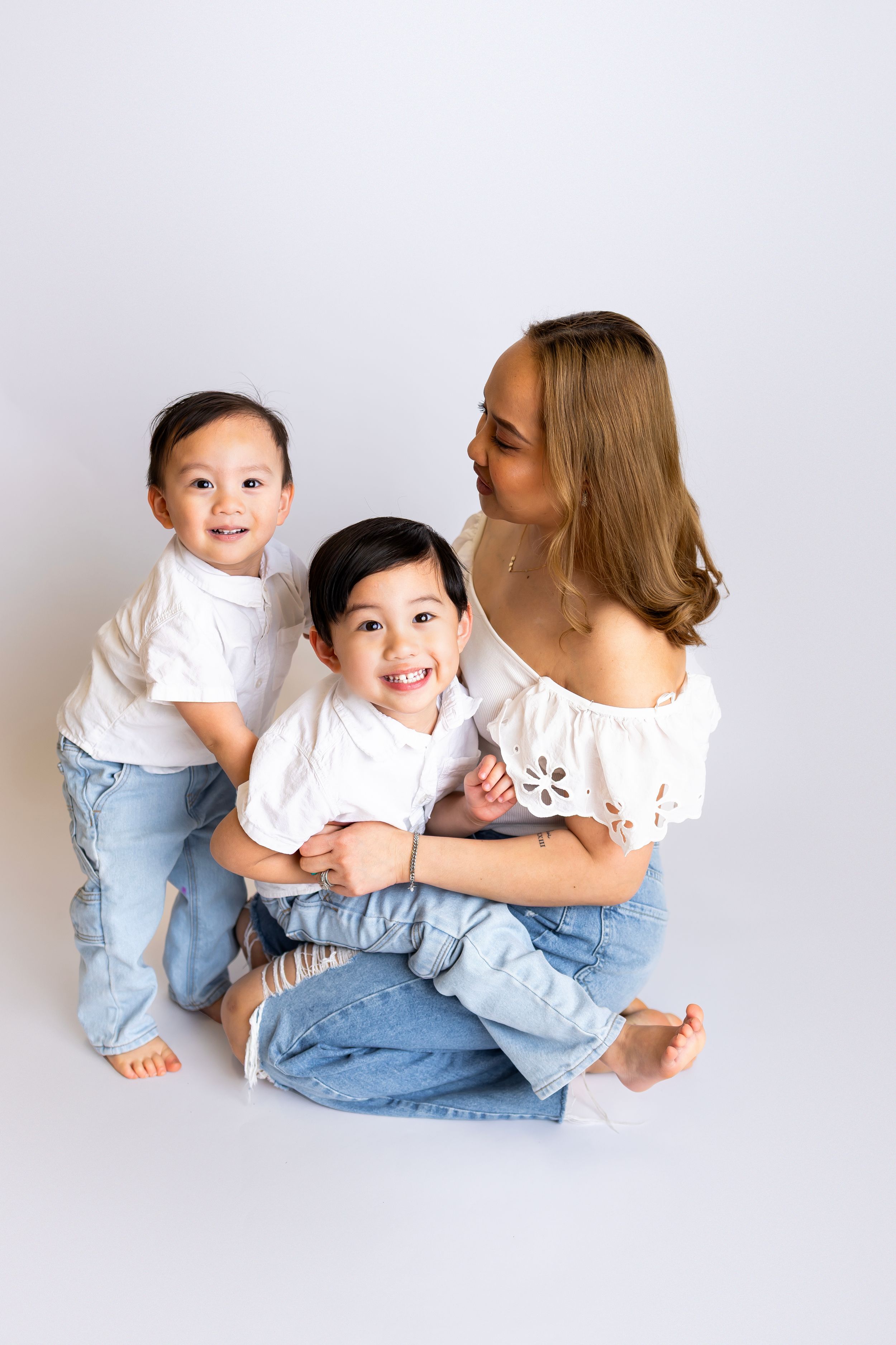 A family in matching white tops and jeans sits together on a white background, sharing joyful smiles and laughter.
