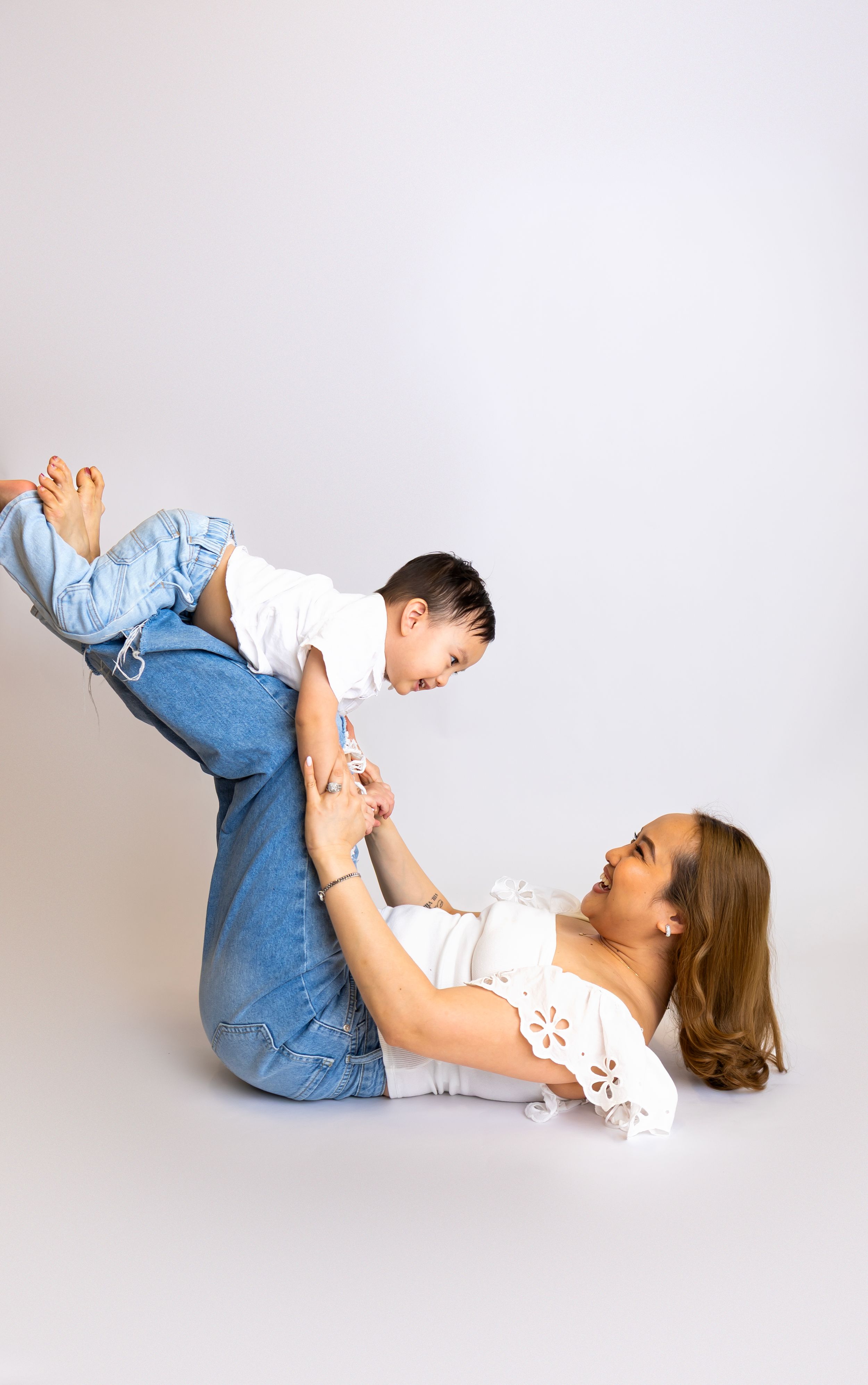 A family plays and bonds together on a light gray studio backdrop, with playful lifting poses in casual attire.