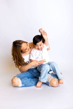 A playful moment between a parent and small child sitting together on a white background.