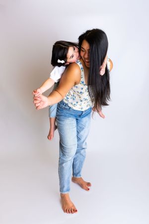 Two people share a playful moment in casual outfits against a light background, one giving a piggyback ride to the other.