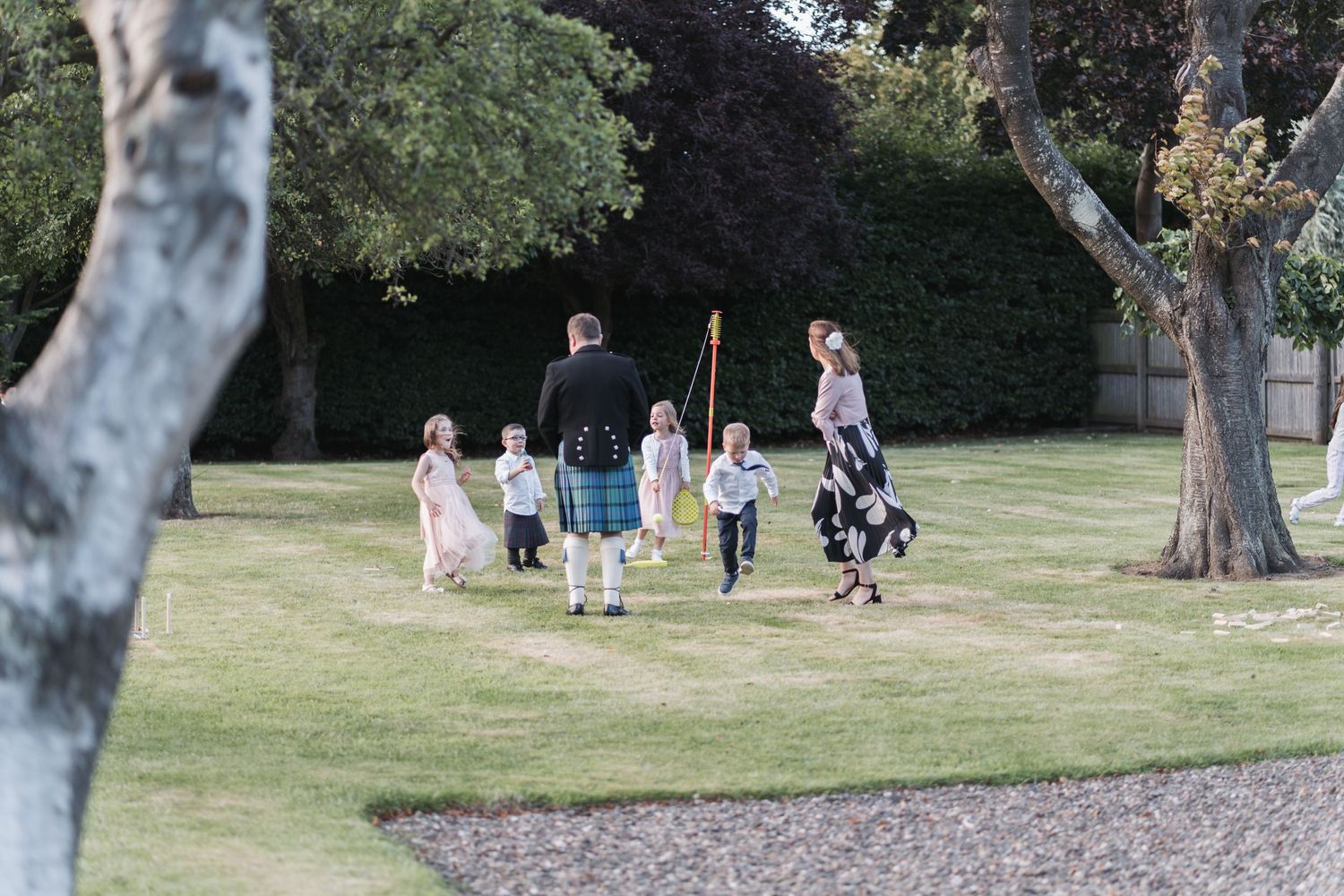 A group walks together across a grassy park area between trees on a sunny day.