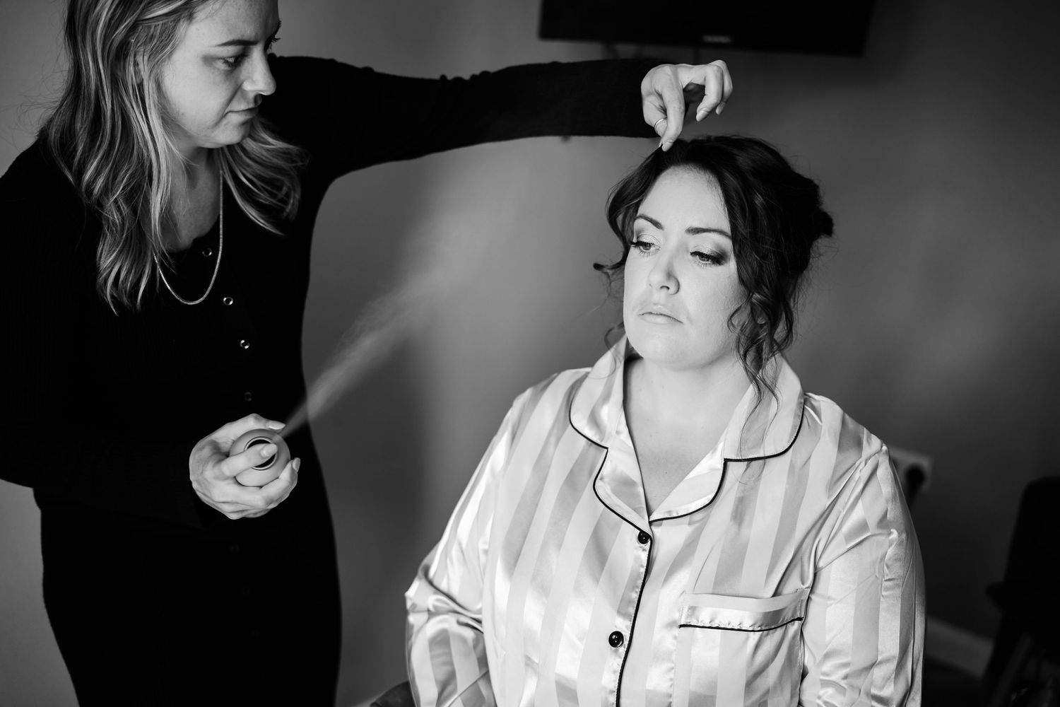 A stylist works on final preparations with someone wearing a white silk pajama-style top in black and white photography.