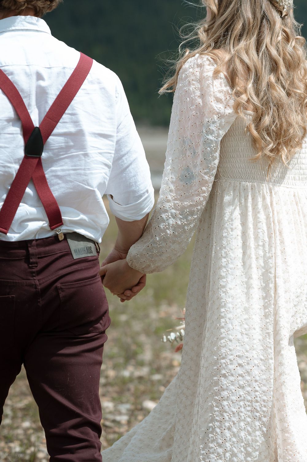 A close-up of couple holding hands, showing white lace dress and red suspenders details.