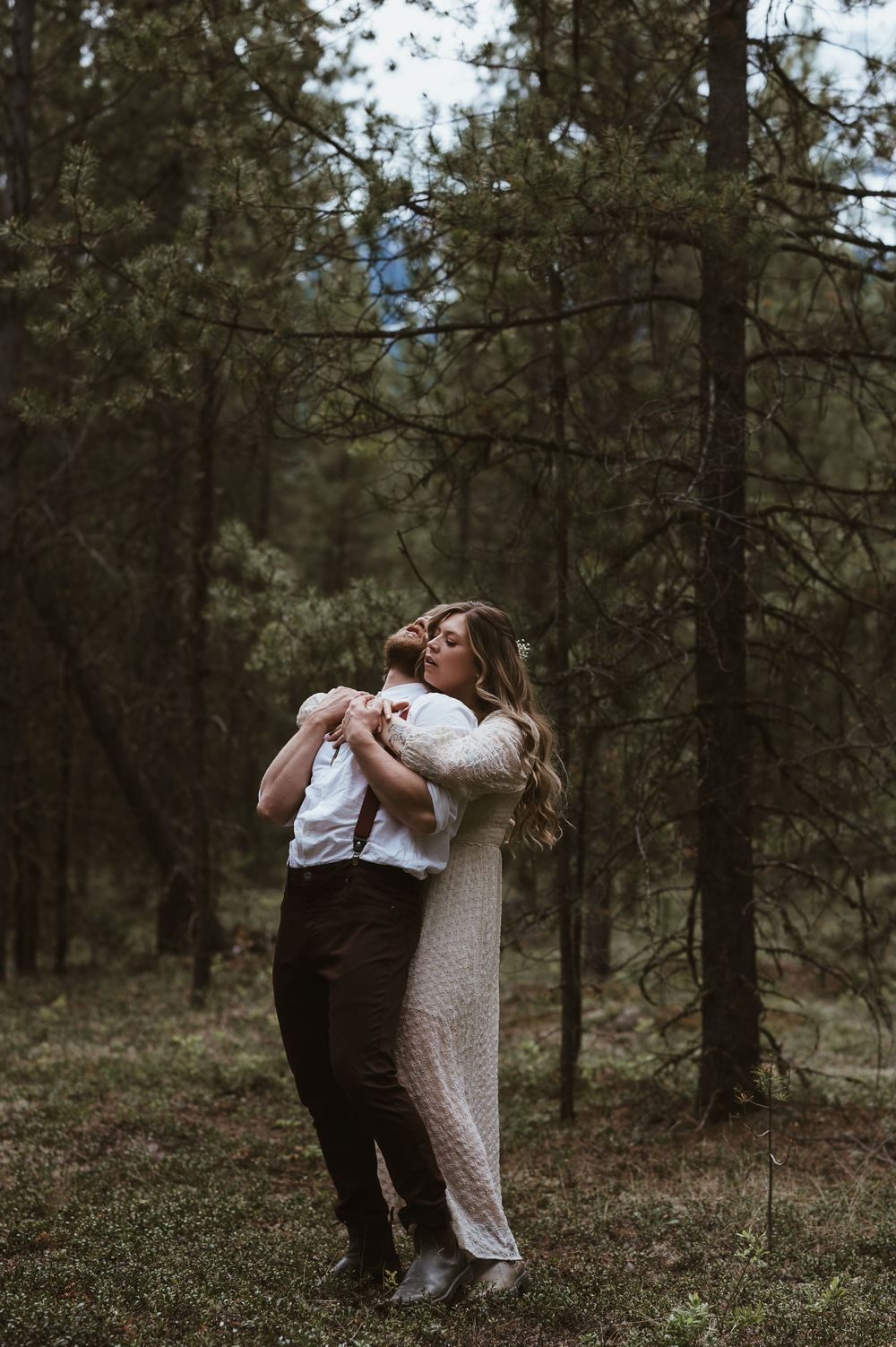 A romantic embrace among pine trees during a mountain wedding photoshoot.