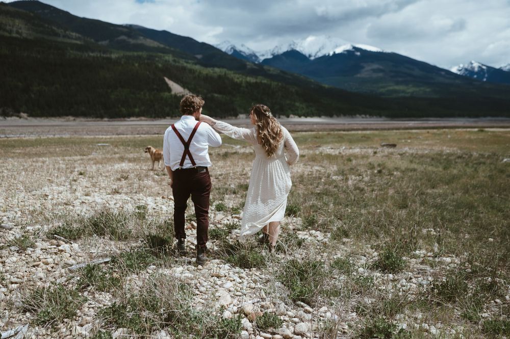 A couple dances in a mountain meadow, with snow-capped peaks in the distance.