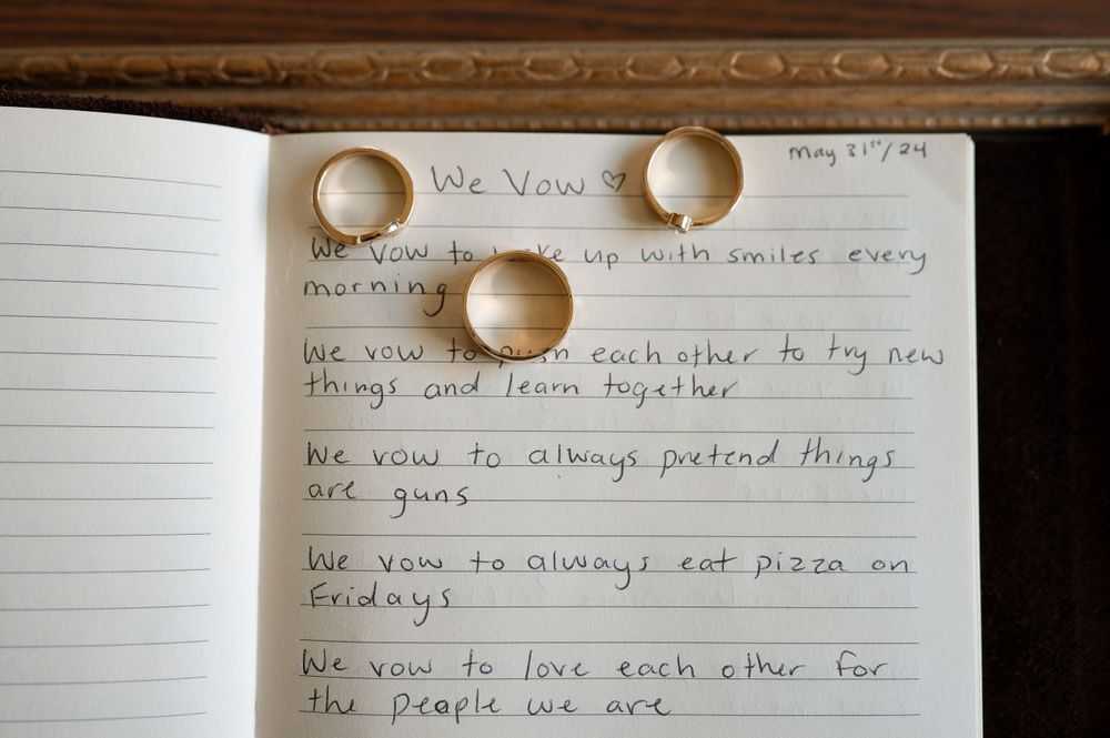 Three wedding rings arranged on handwritten vows in a notebook.