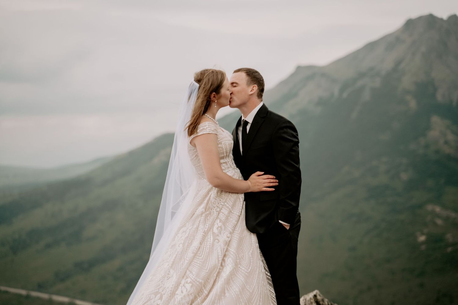 A couple embraces against a backdrop of misty mountains during their wedding.